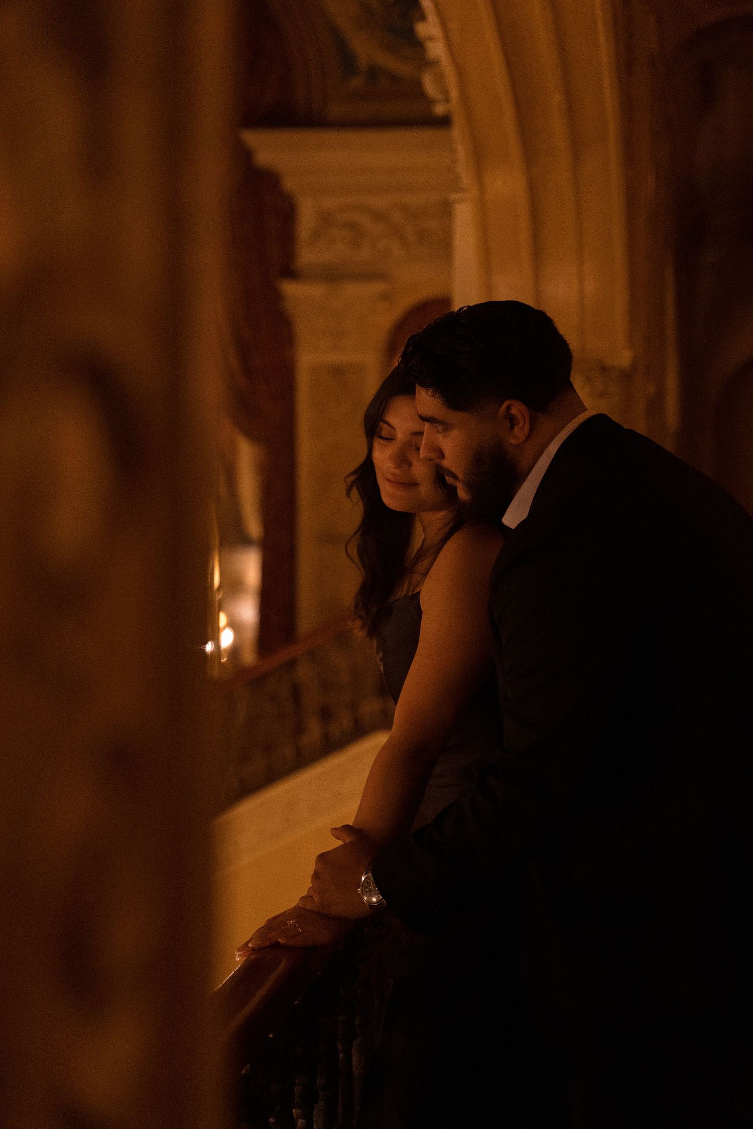 A romantic couple shares an intimate moment in a dimly lit historic ballroom.