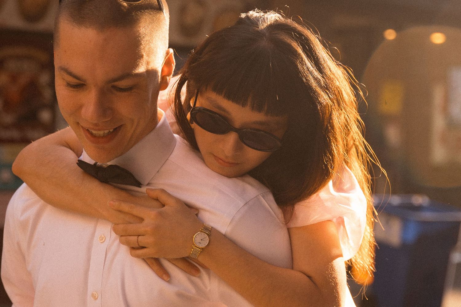 A romantic couple in formal attire embracing in warm sunset lighting.