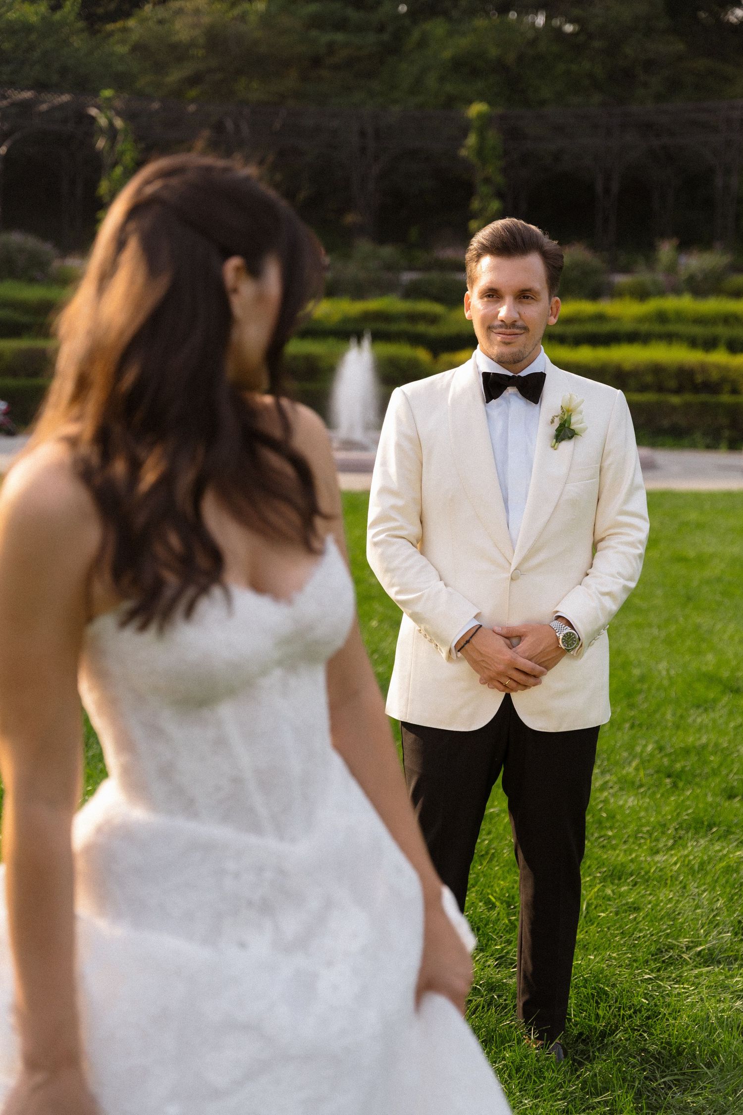 A wedding couple poses in a garden setting with the groom wearing a white dinner jacket and black bow tie.