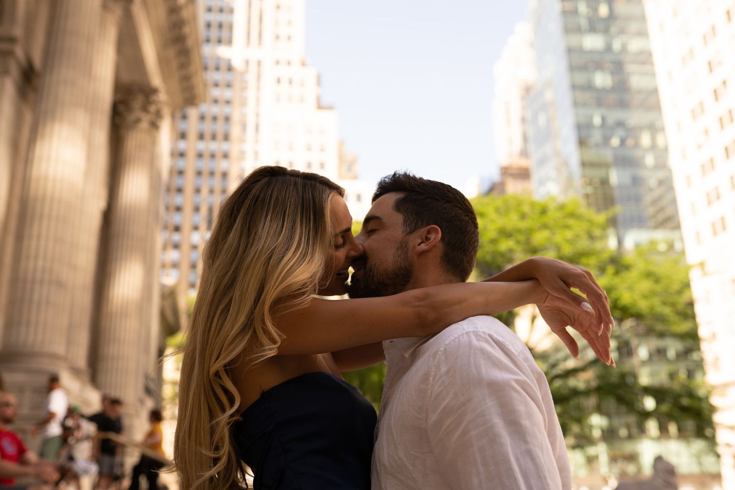 Romantic sequence under classical stone columns with city buildings in background.