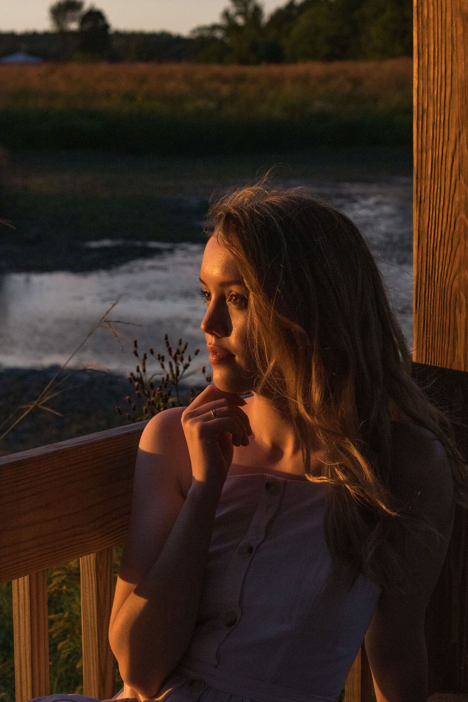 Silhouette of someone gazing at sunset from a wooden porch overlooking water.