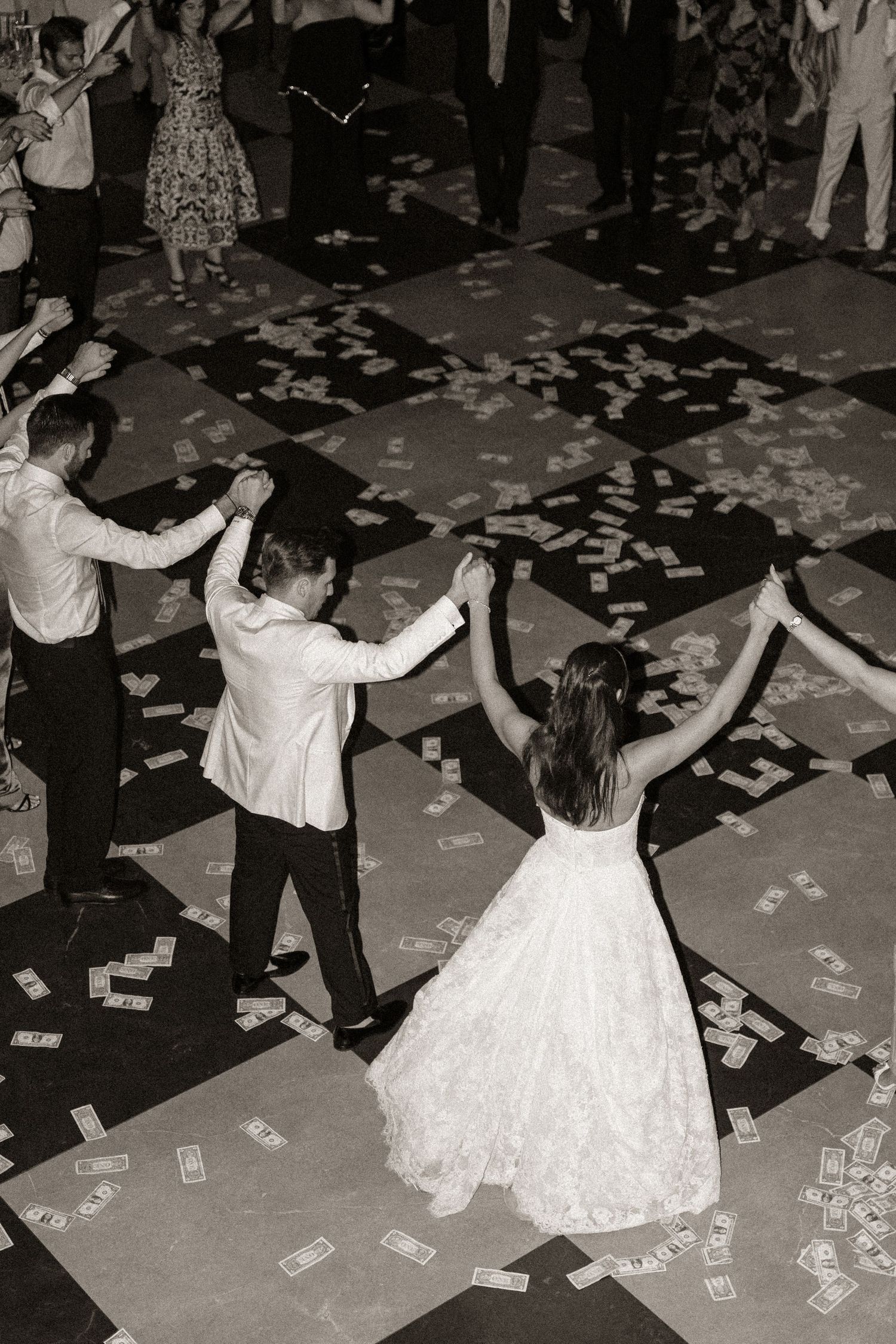 Wedding guests dancing and celebrating on a dance floor covered in scattered money and confetti.