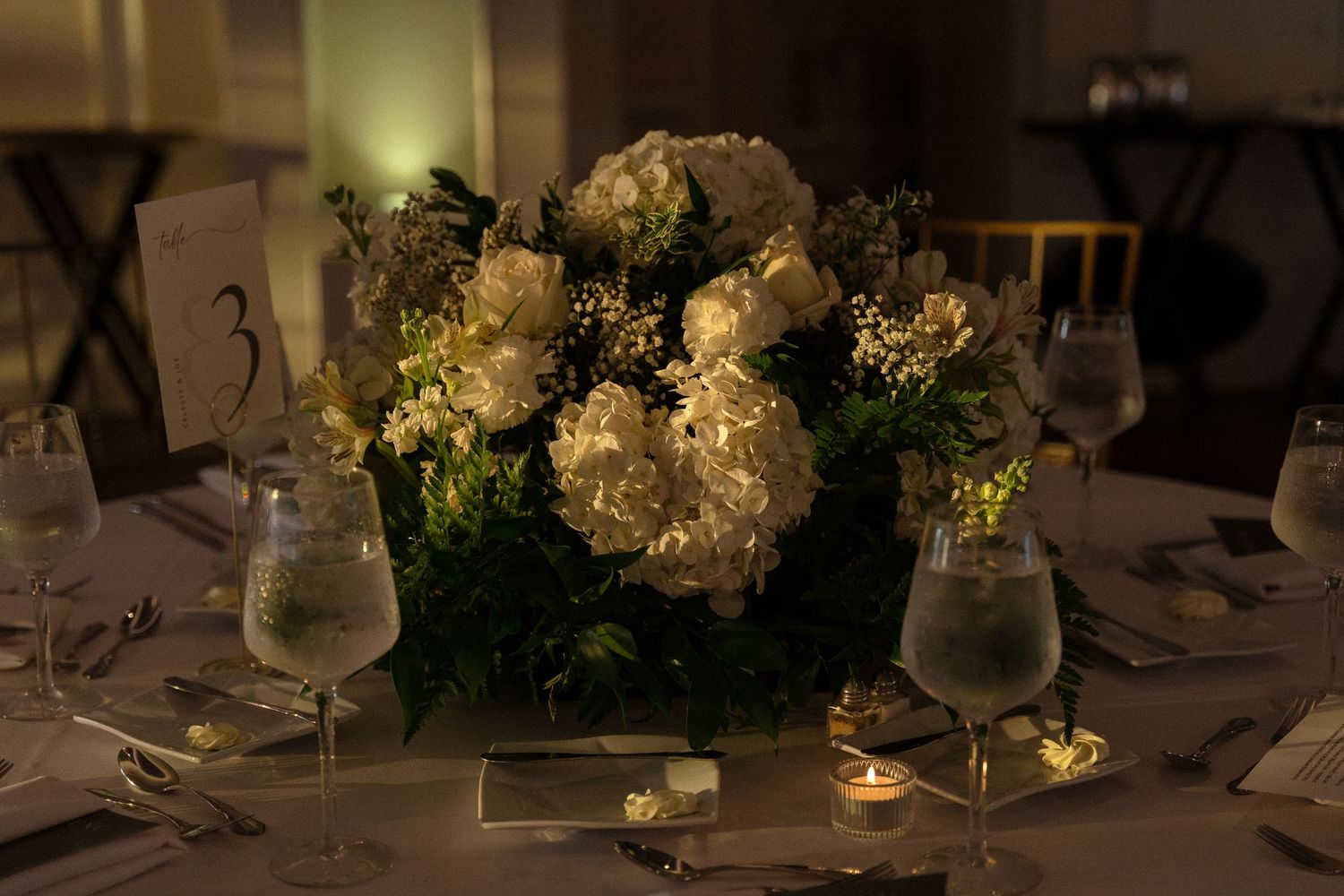 Elegant wedding reception table with white floral centerpieces and ambient lighting.