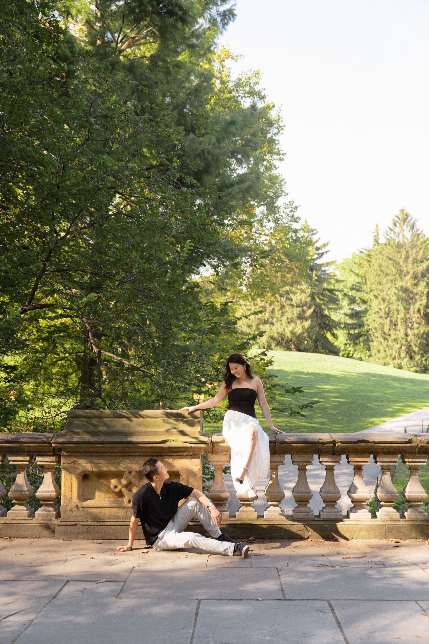 A couple relaxes on stone balustrades in a sunny garden setting.