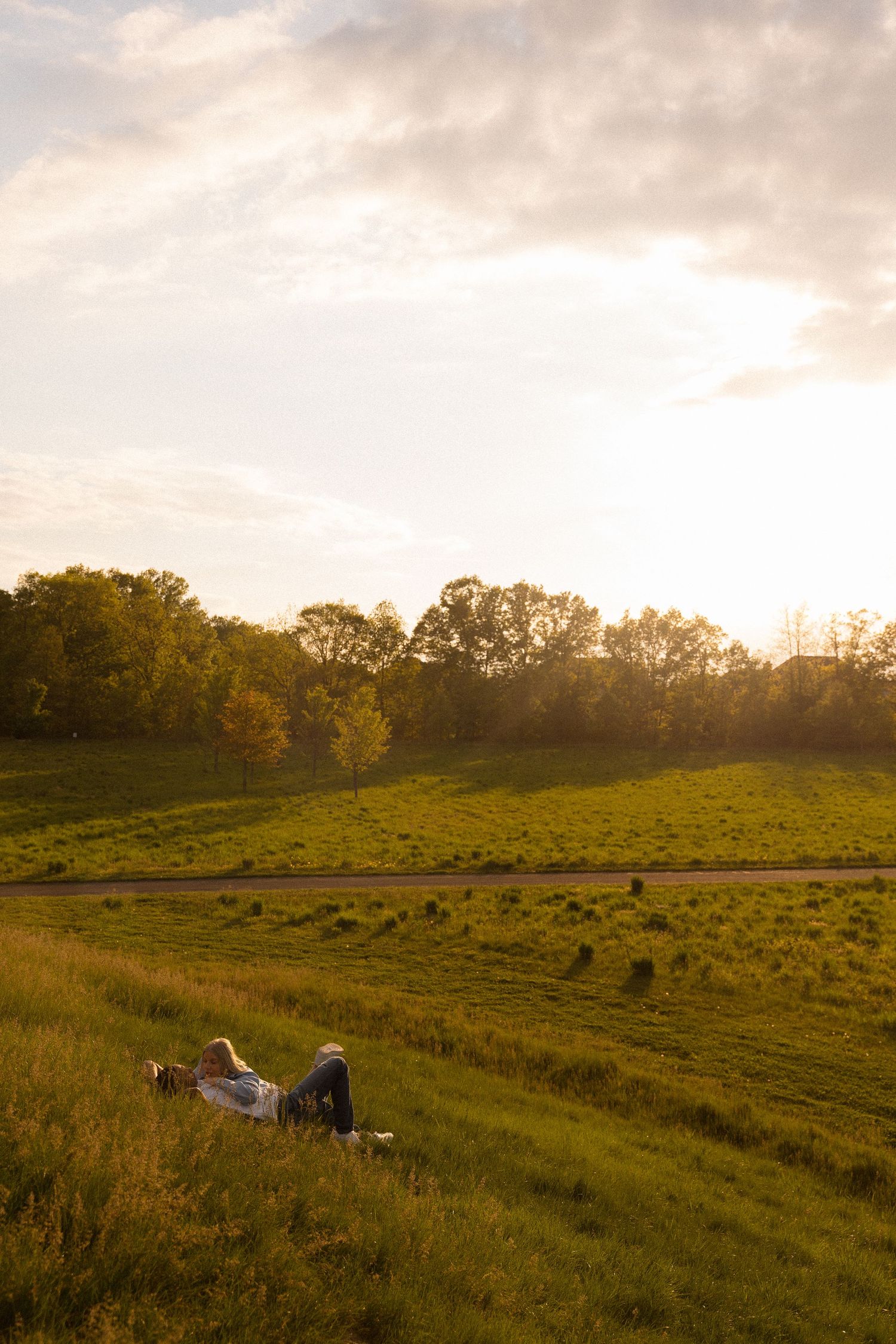 A couple relaxes on a grassy hillside during golden hour sunset.
