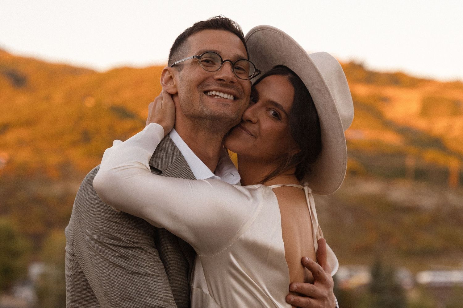 Couple embracing during golden hour sunset against mountain backdrop.
