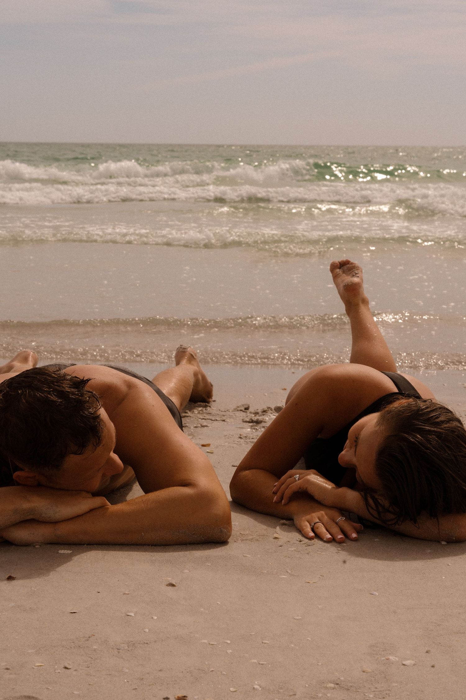 Couple lying together on a sandy beach at sunset in an artistic black and white photo series.