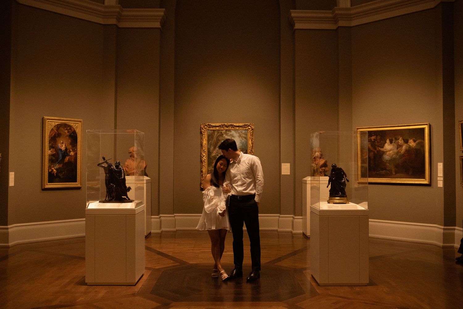 Multiple views of a dimly lit museum gallery with classical artwork and ornate architectural details.