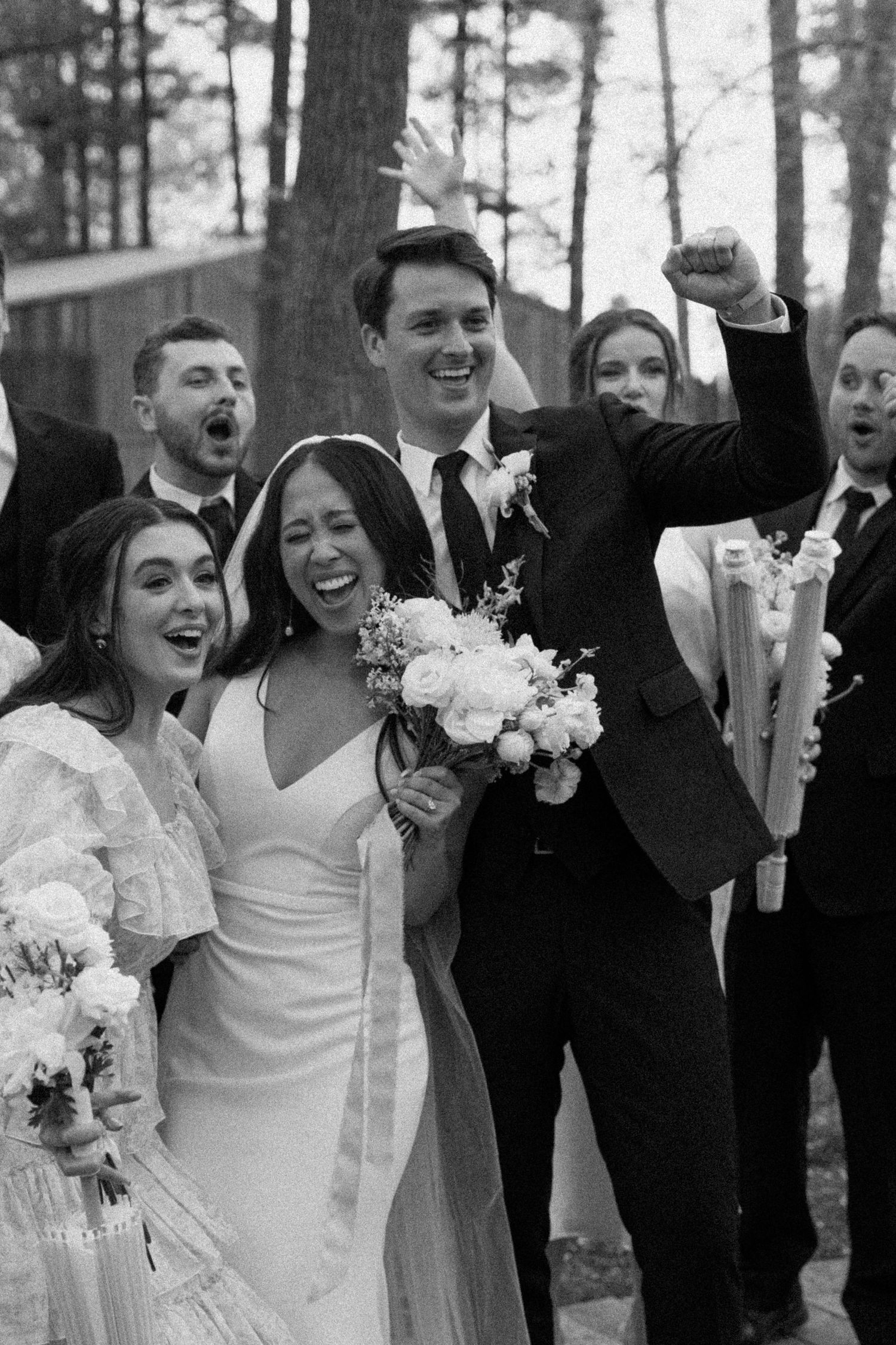 Wedding party celebrates joyfully together in black and white forest portrait.