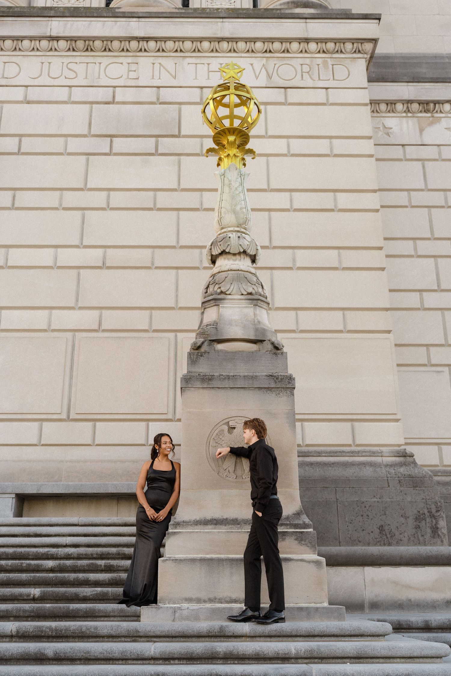 A couple poses dramatically on stone steps near an ornate golden architectural detail.