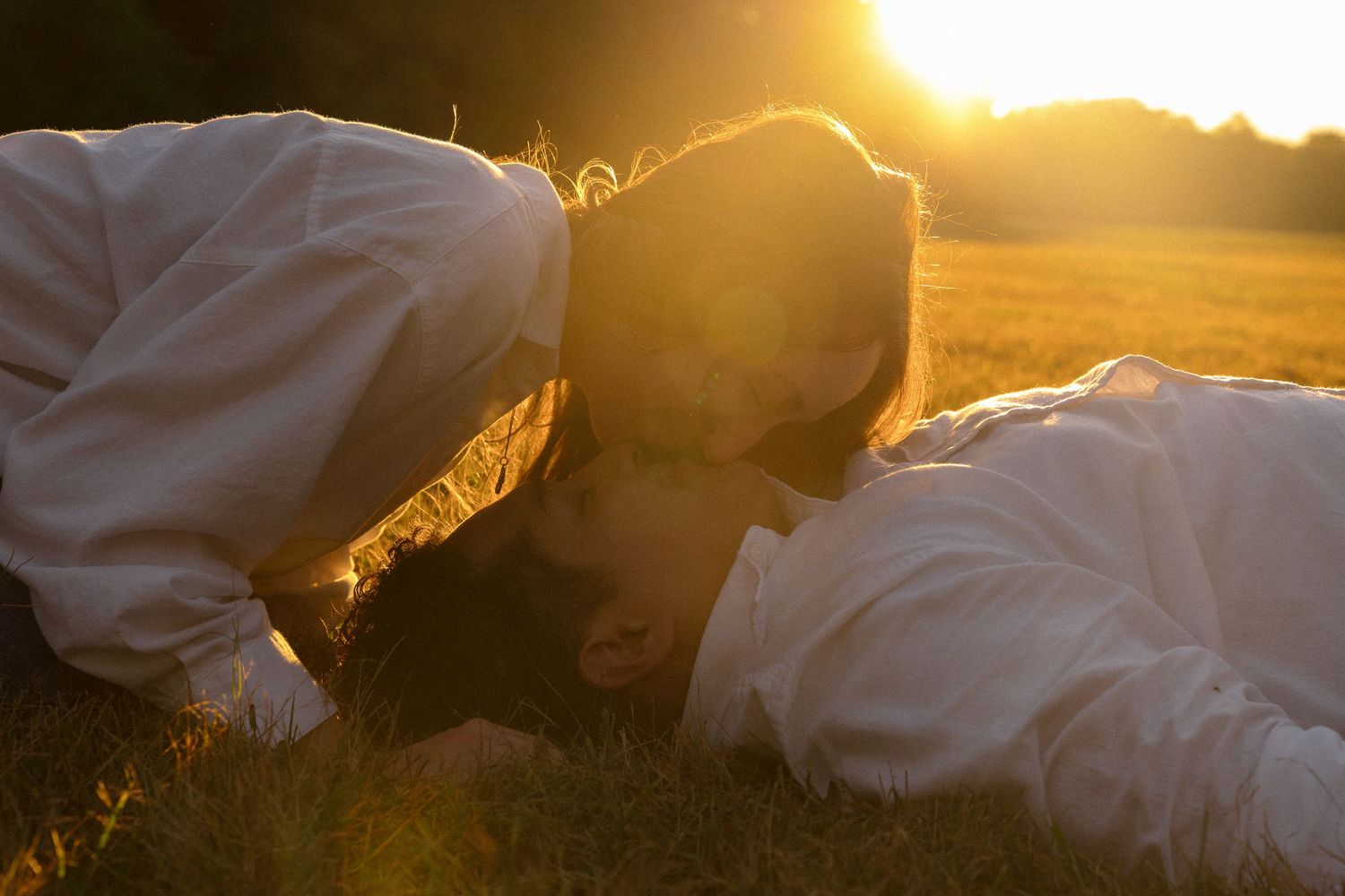 Two people in white clothing share an intimate moment in golden sunlight.