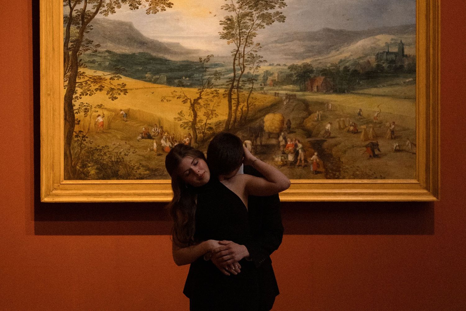 Landscape paintings hang on terracotta walls in an elegant museum gallery.