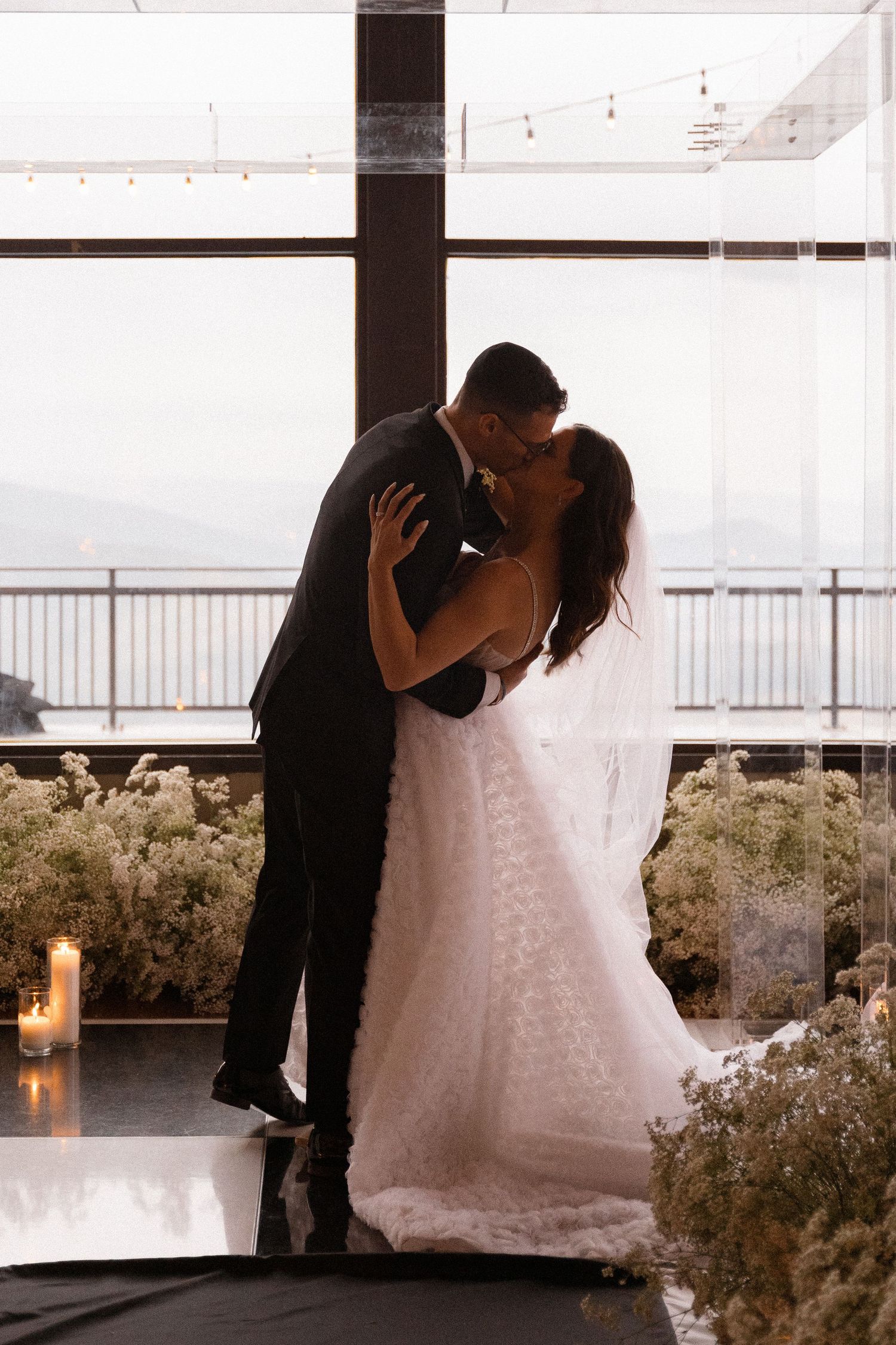 Romantic silhouettes of a couple embracing in front of large windows.
