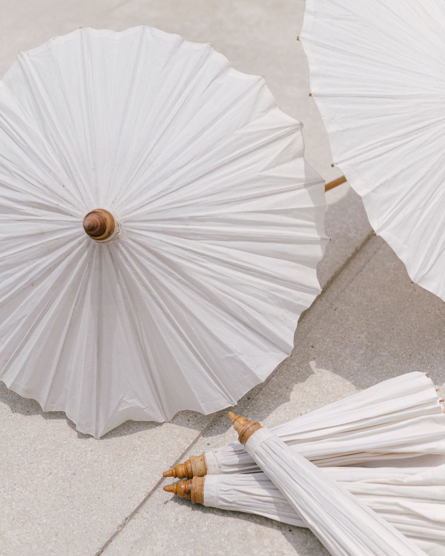 White paper parasols with bamboo handles displayed on a concrete surface, perfect for weddings or outdoor events.