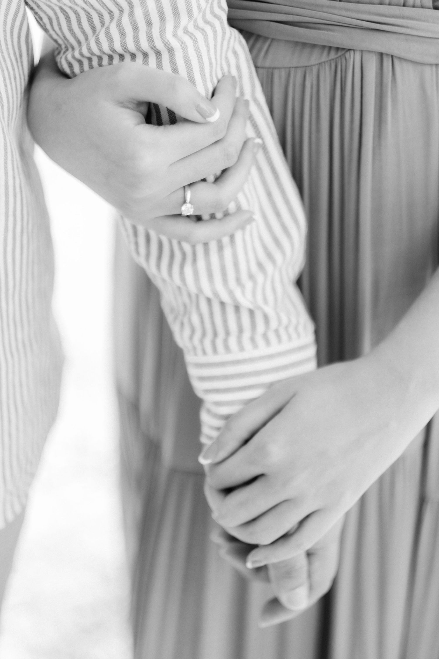 Black and white photo of a couple holding hands, woman wearing an engagement ring, close-up romantic detail shot.