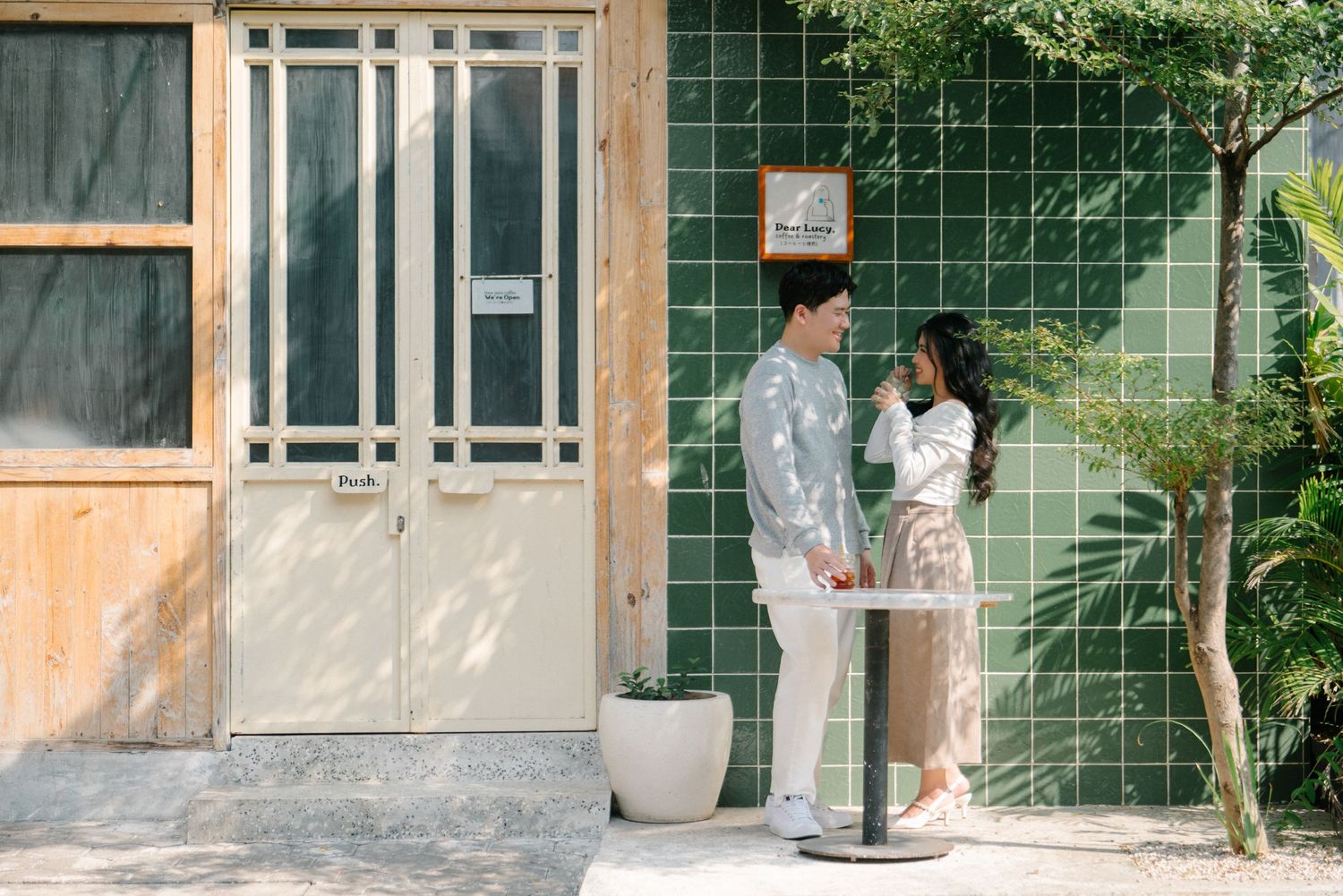 Couple standing at a tall table outside a cafe with green tiled walls and wooden doors.