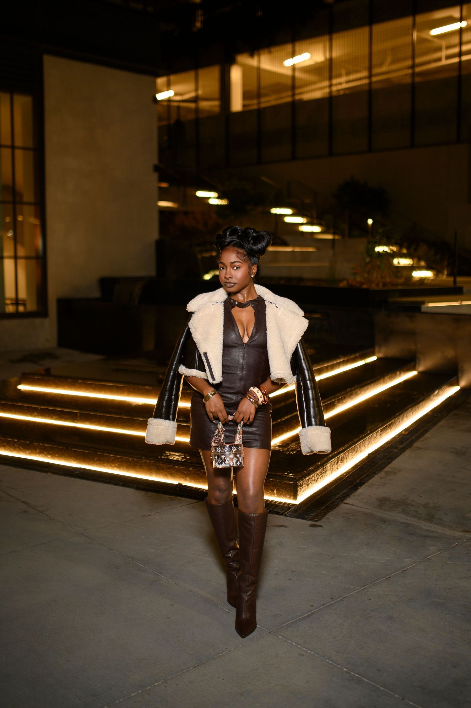 Woman in fur-trim jacket and leather mini dress outdoors at night.