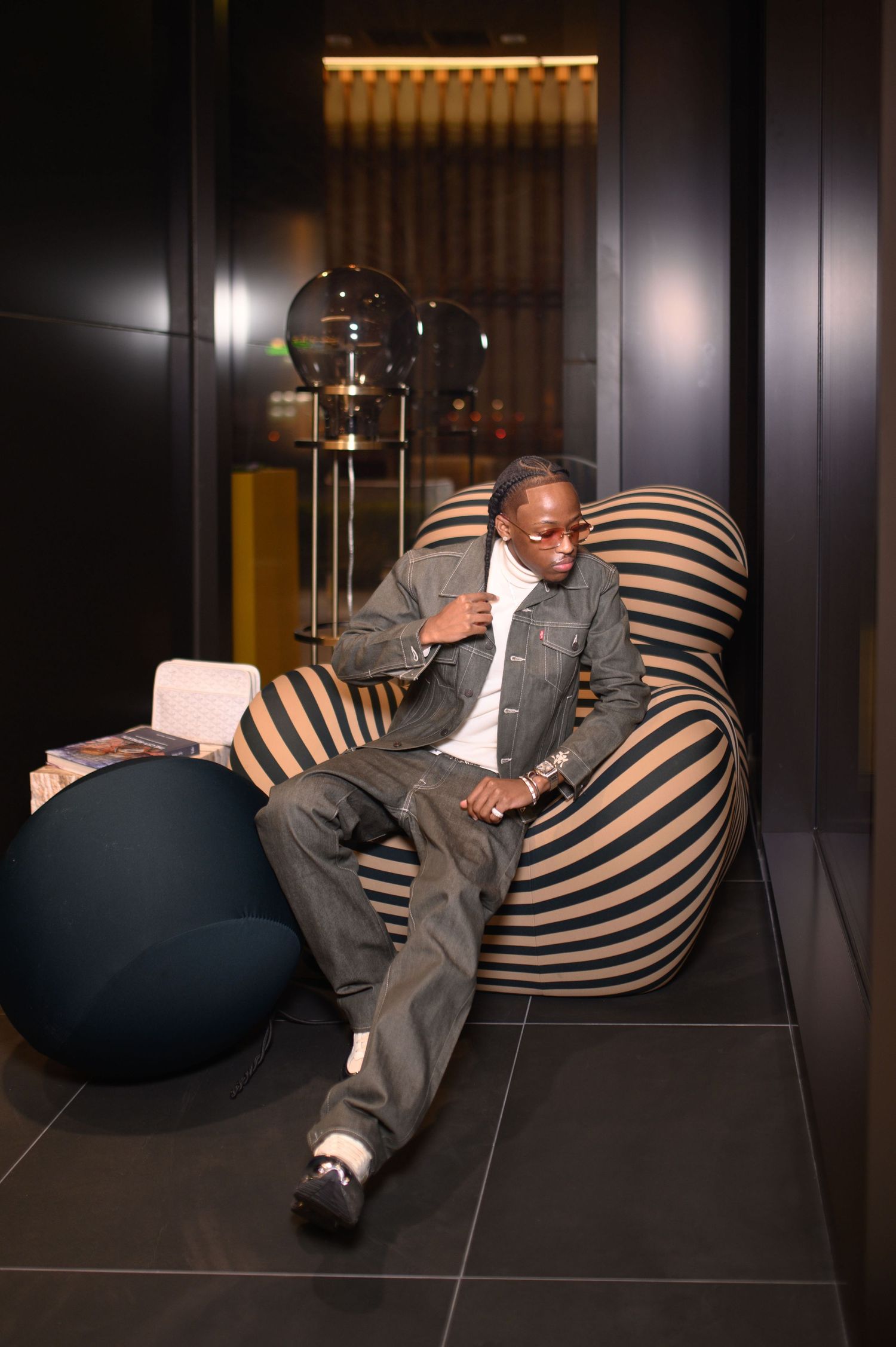Man in denim jacket relaxing in striped bean bag chair indoors.