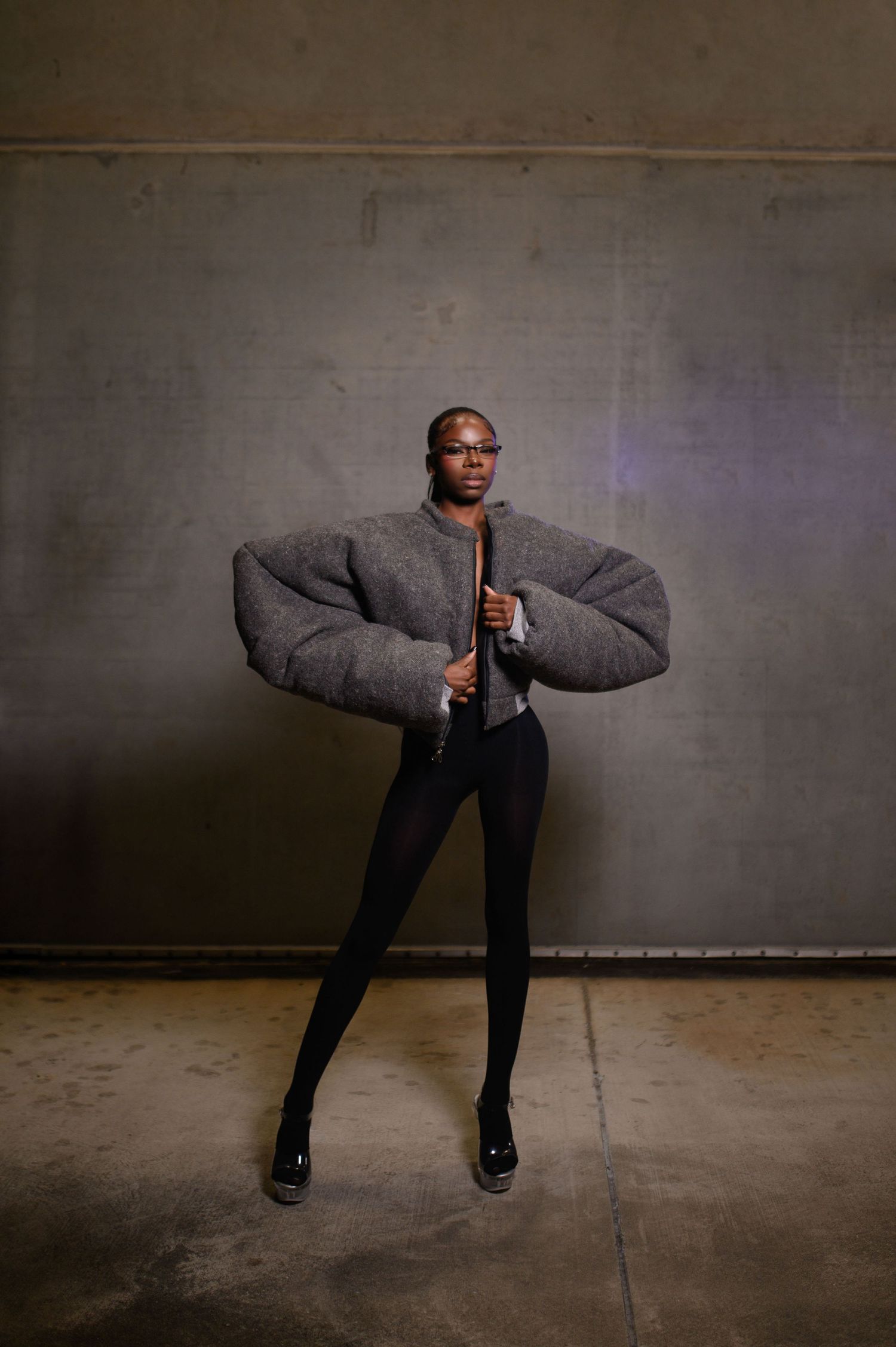 Model wearing dramatic oversized gray puffer jacket with black leggings in studio.