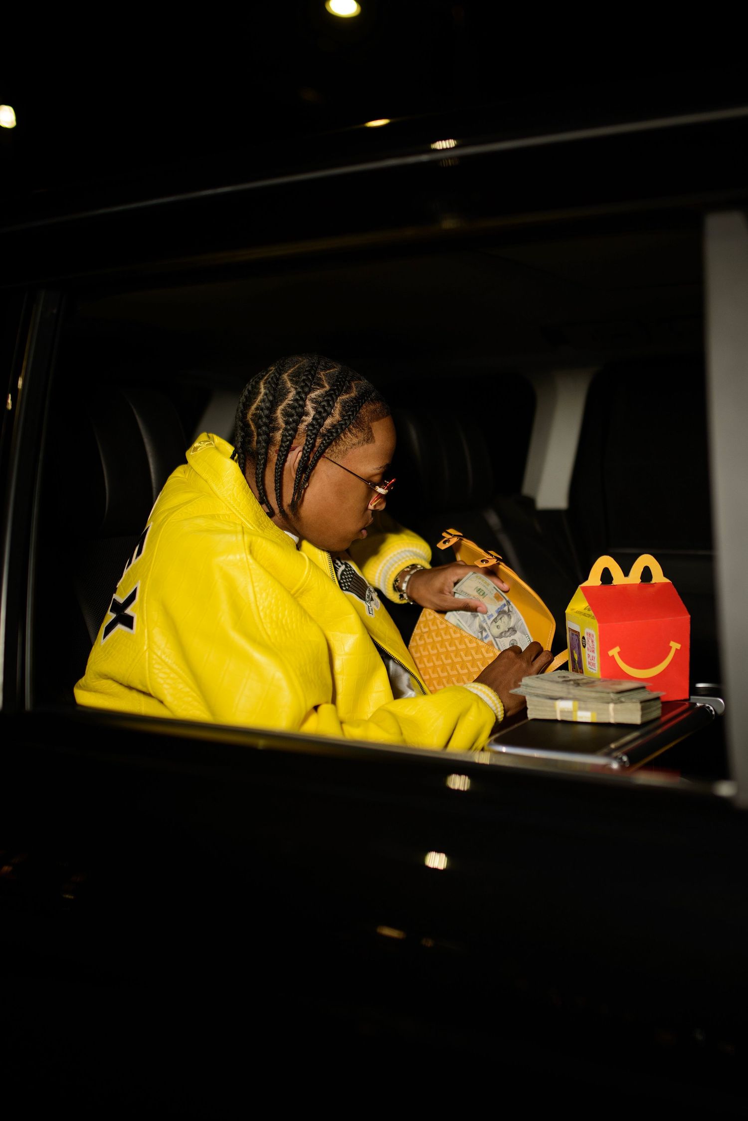 Person in yellow leather jacket cradling a newborn baby inside a dark vehicle next to a Happy Meal.