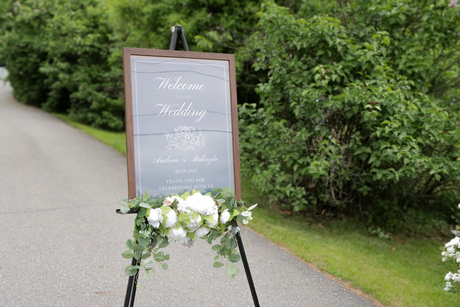 Outdoor wedding signage with white and green florals.