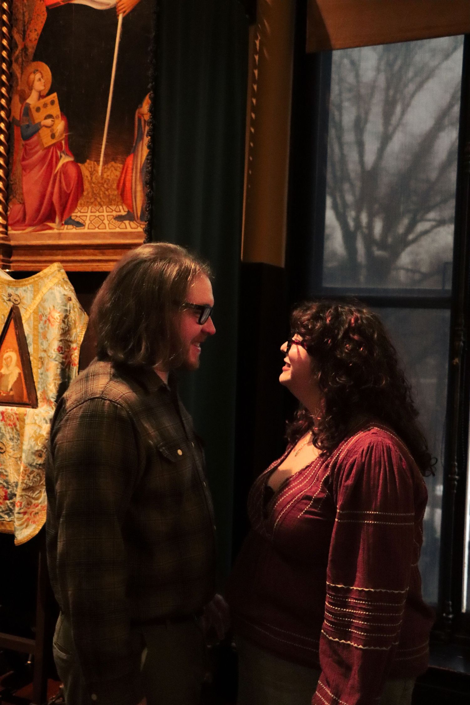 A couple looks at each other in a darkened gallery space with warm lighting in Boston Massachusetts.