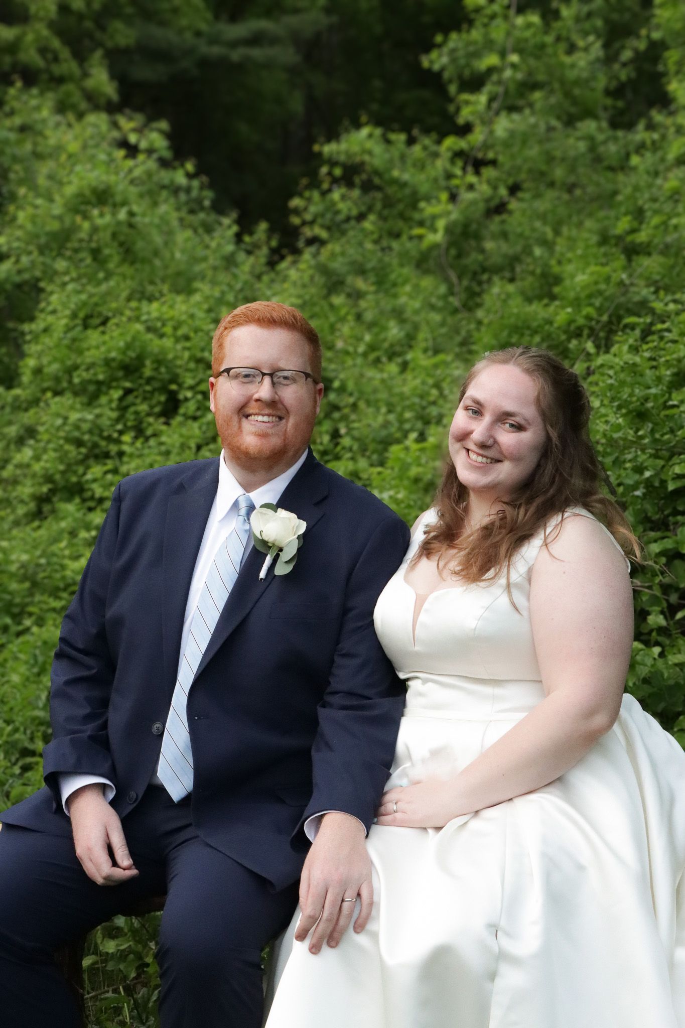 A happy bride and groom share a joyful moment together outdoors surrounded by lush green foliage on their wedding day.