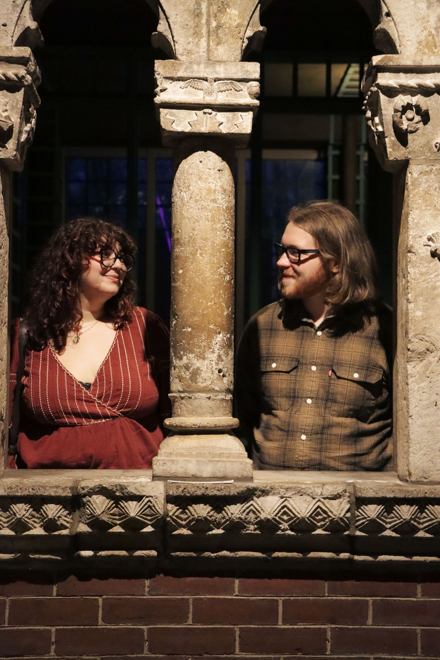 A romantic couple posed at an arched stone windows along a brick wall in a Boston Massachusetts museum.