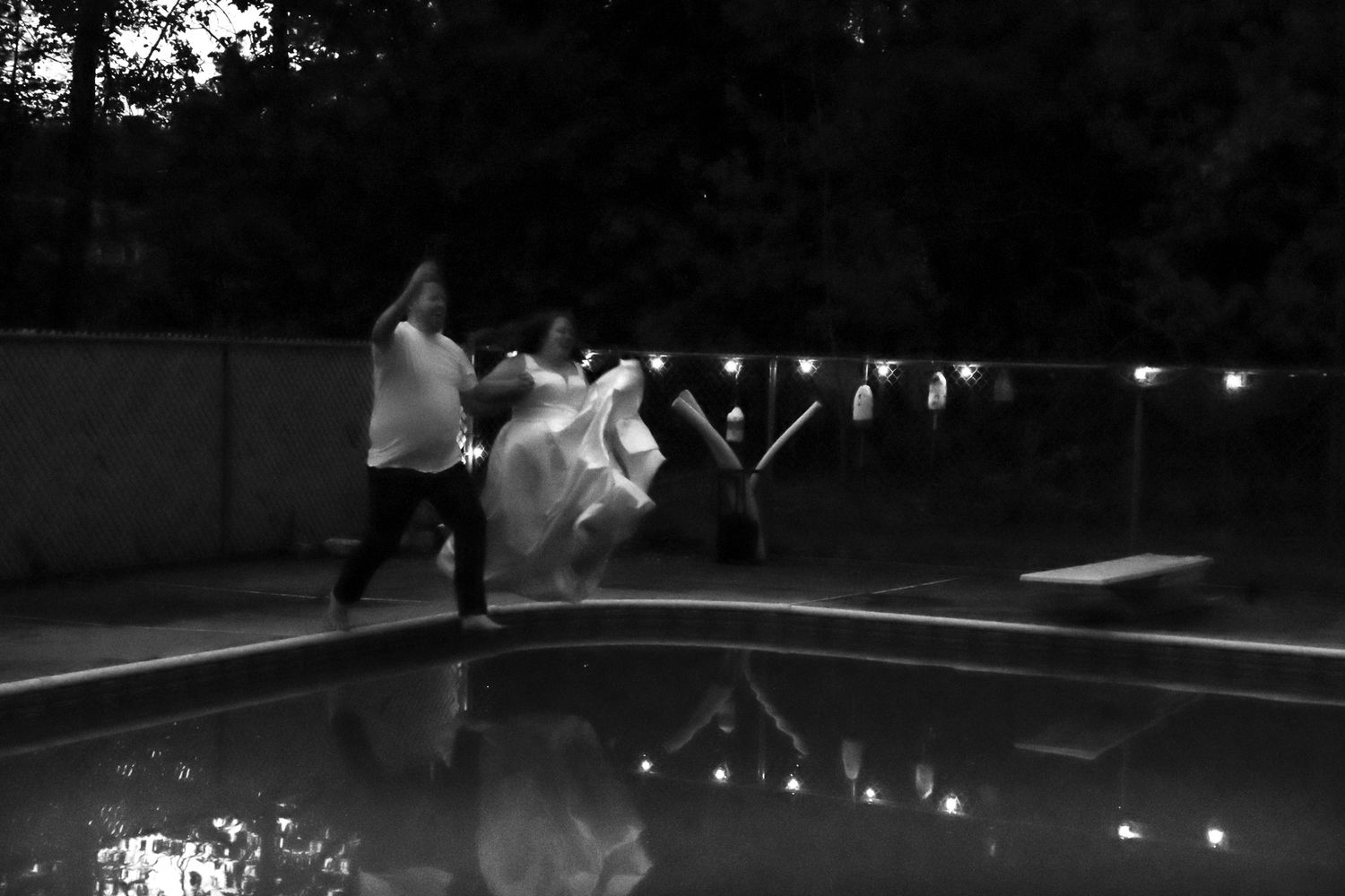 Bride and groom jump into pool during outdoor wedding reception.