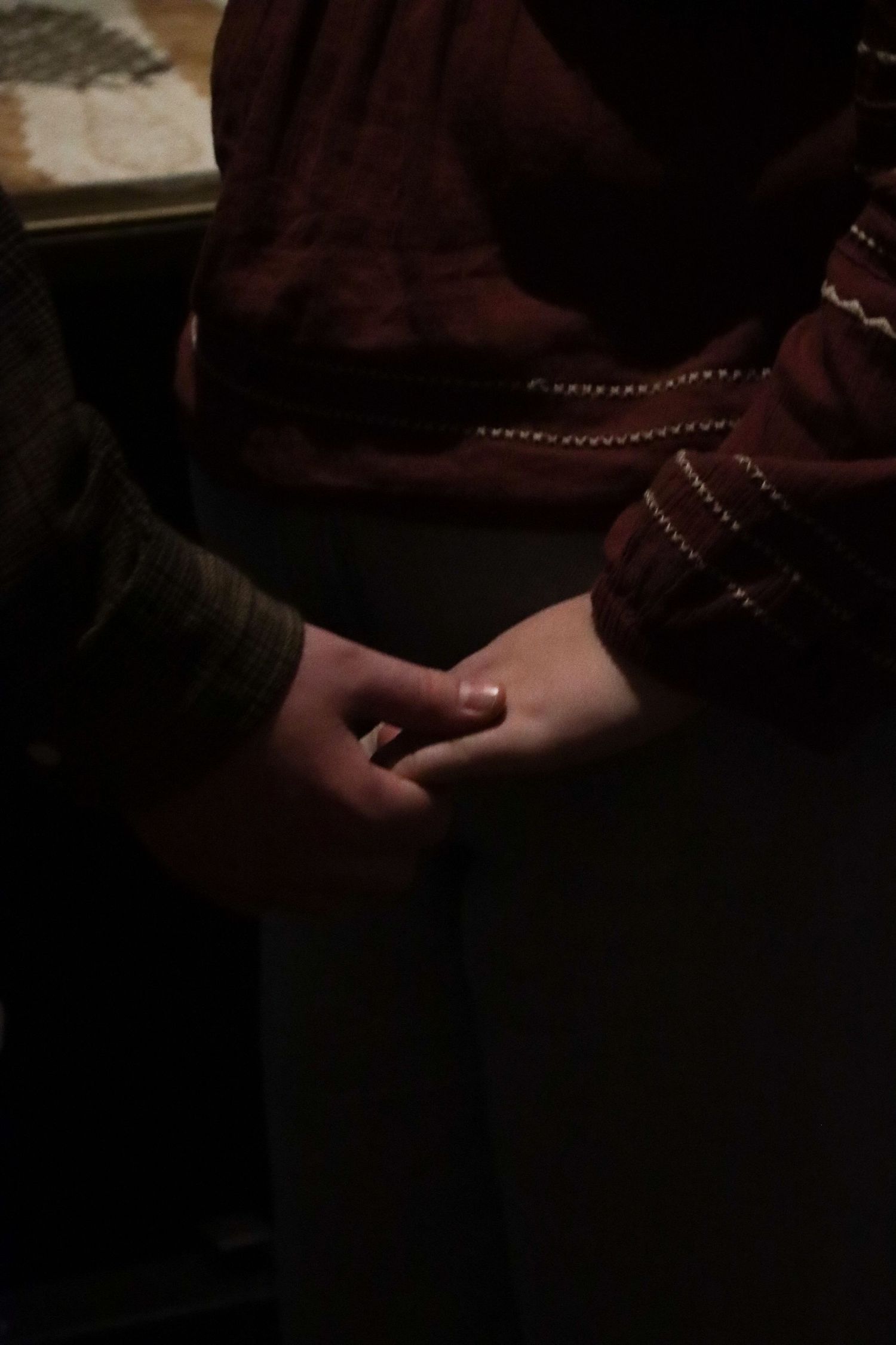 Close-up of a couples gently holding hands in a dark dimly lit setting.