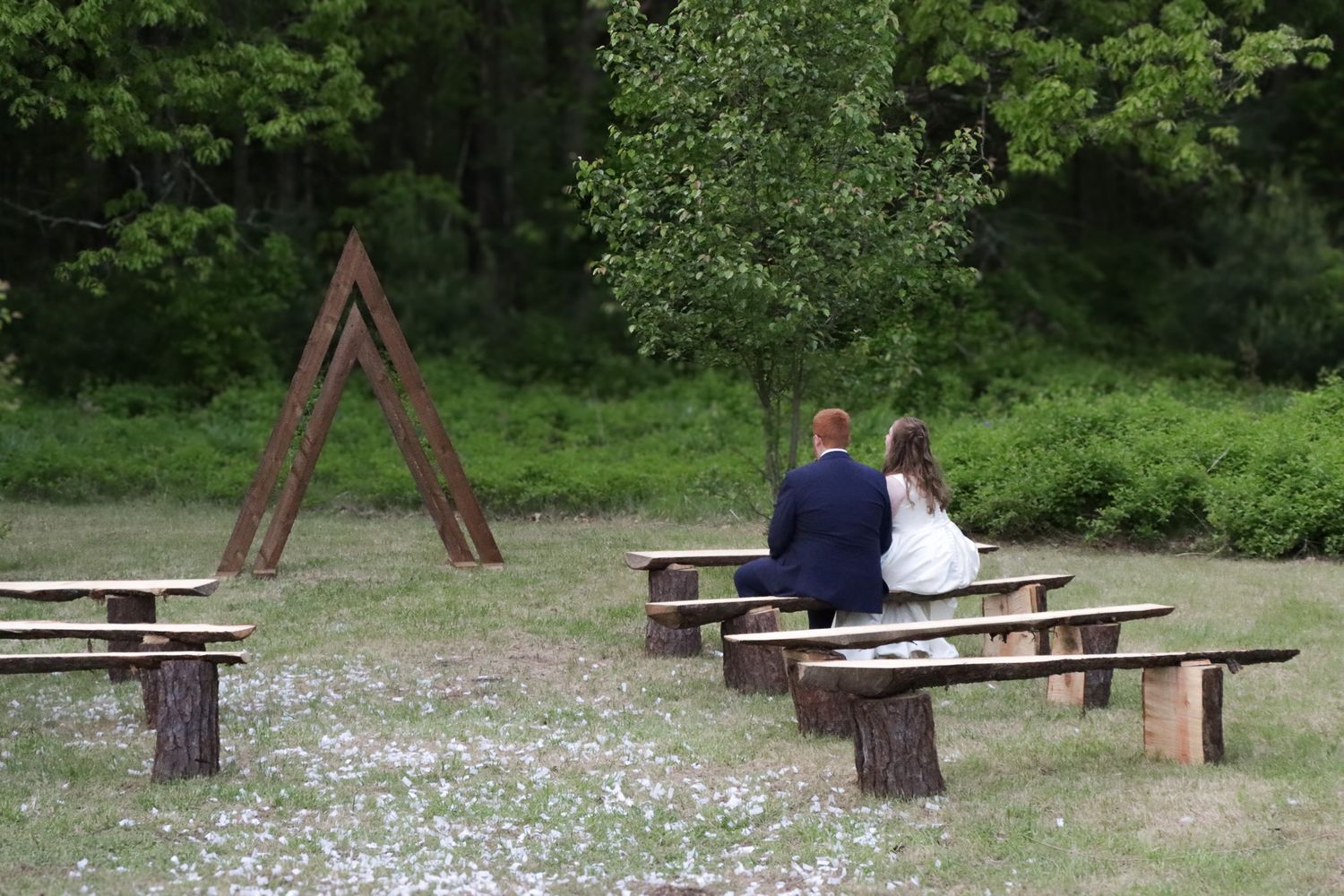 Bride and groom share an intimate moment together sitting on a wooden bench in their wedding ceremony space.
