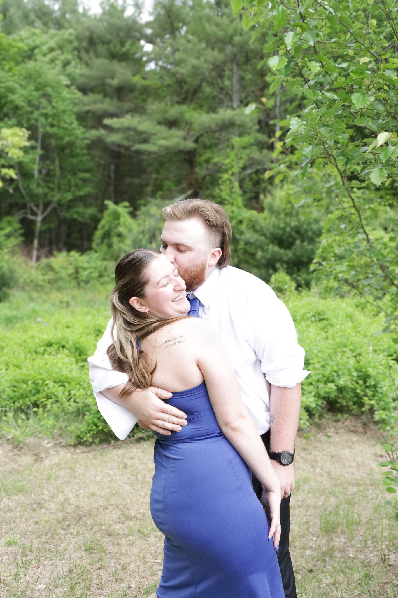 A couple embraces in a romantic moment outdoors surrounded by lush green foliage in a natural setting.
