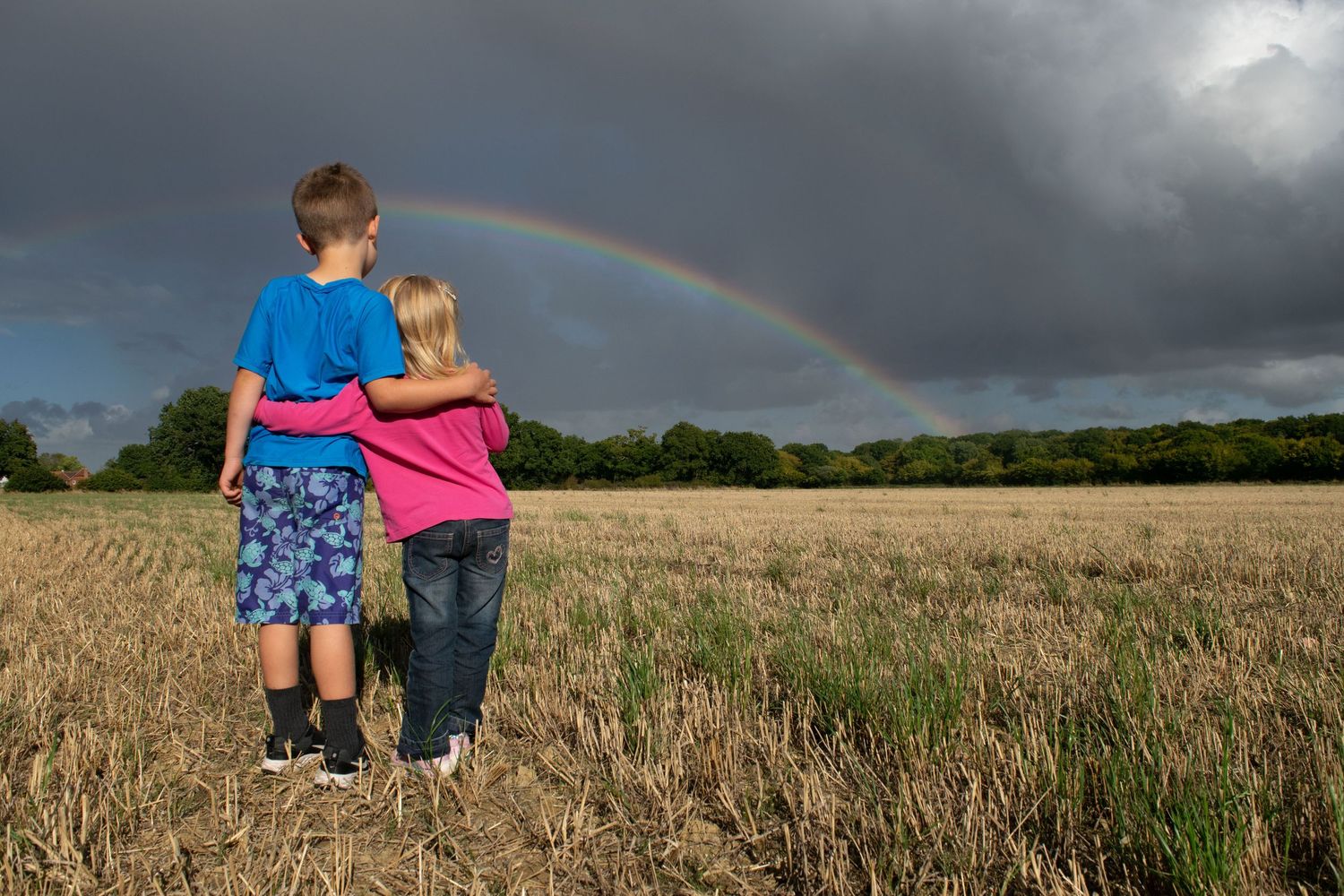 Two young children photographed from behind, hugging and watching the rainbow in a stromy skye, Kent photography