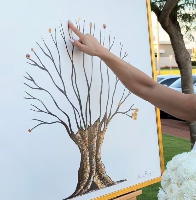 A hand pressing a fingerprint onto a decorative wedding guest book tree painting on a white canvas.
