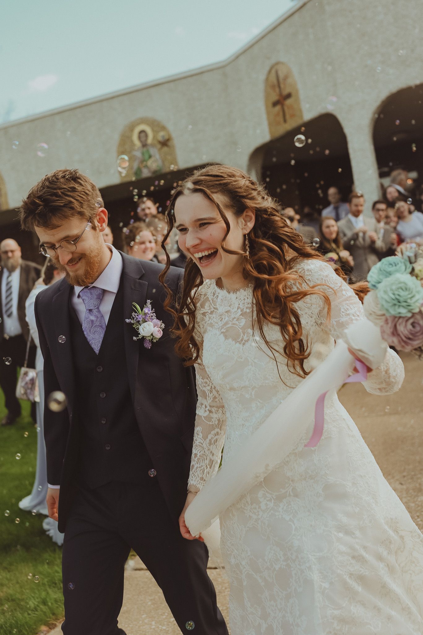 Newlywed couple walks joyfully on their wedding day surrounded by guests.