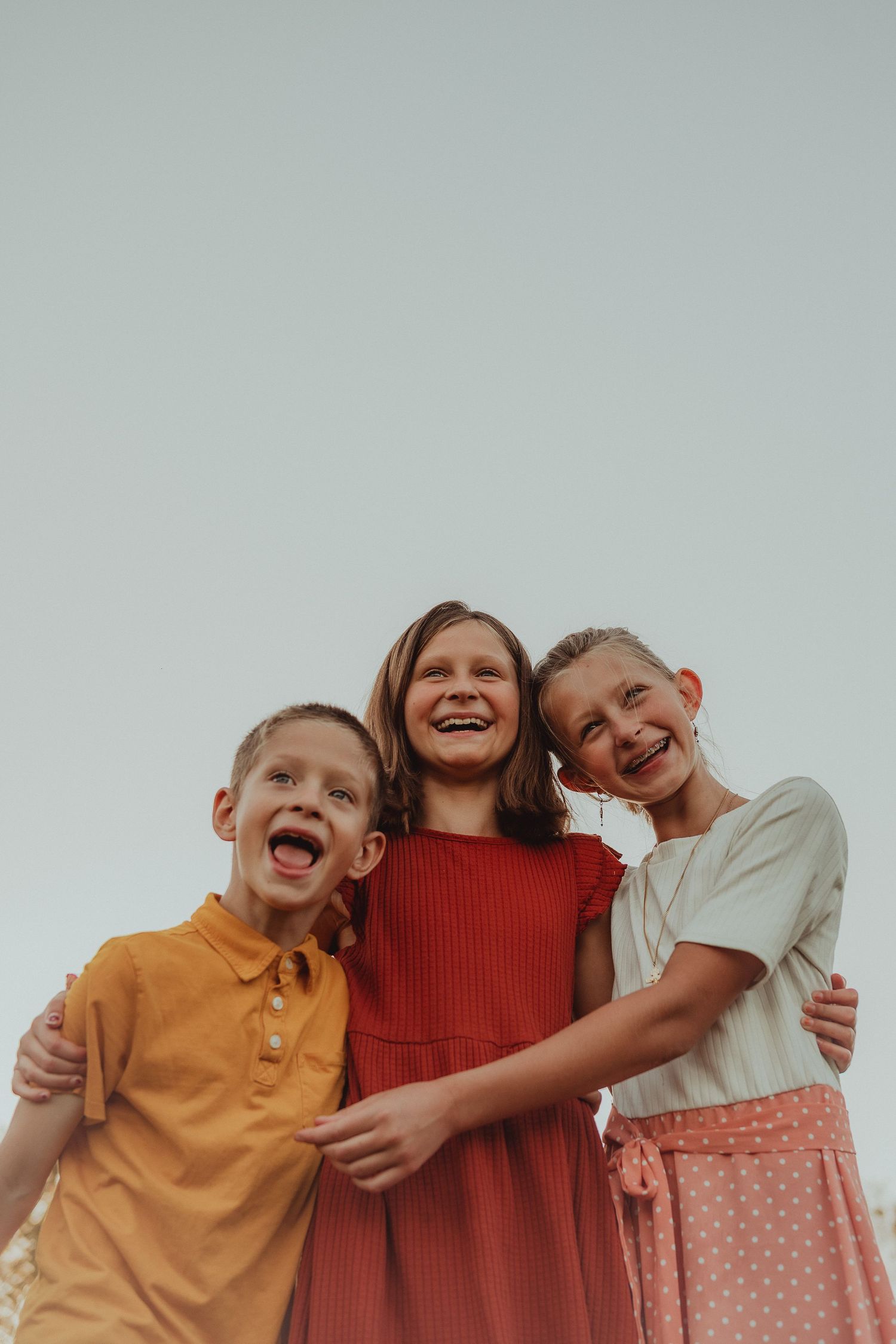 A series of four candid photos showing children laughing and hugging while wearing casual clothing against a light background.