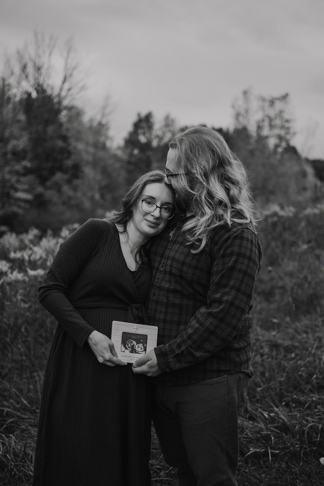 A couple sharing an intimate moment while holding an ultrasound photo outdoors.