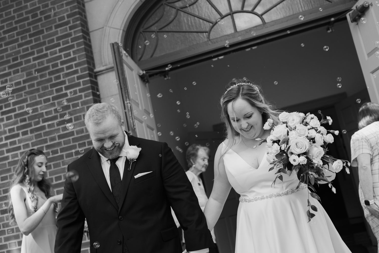 Wedding party celebration sequence outside a brick building with white floral decorations.