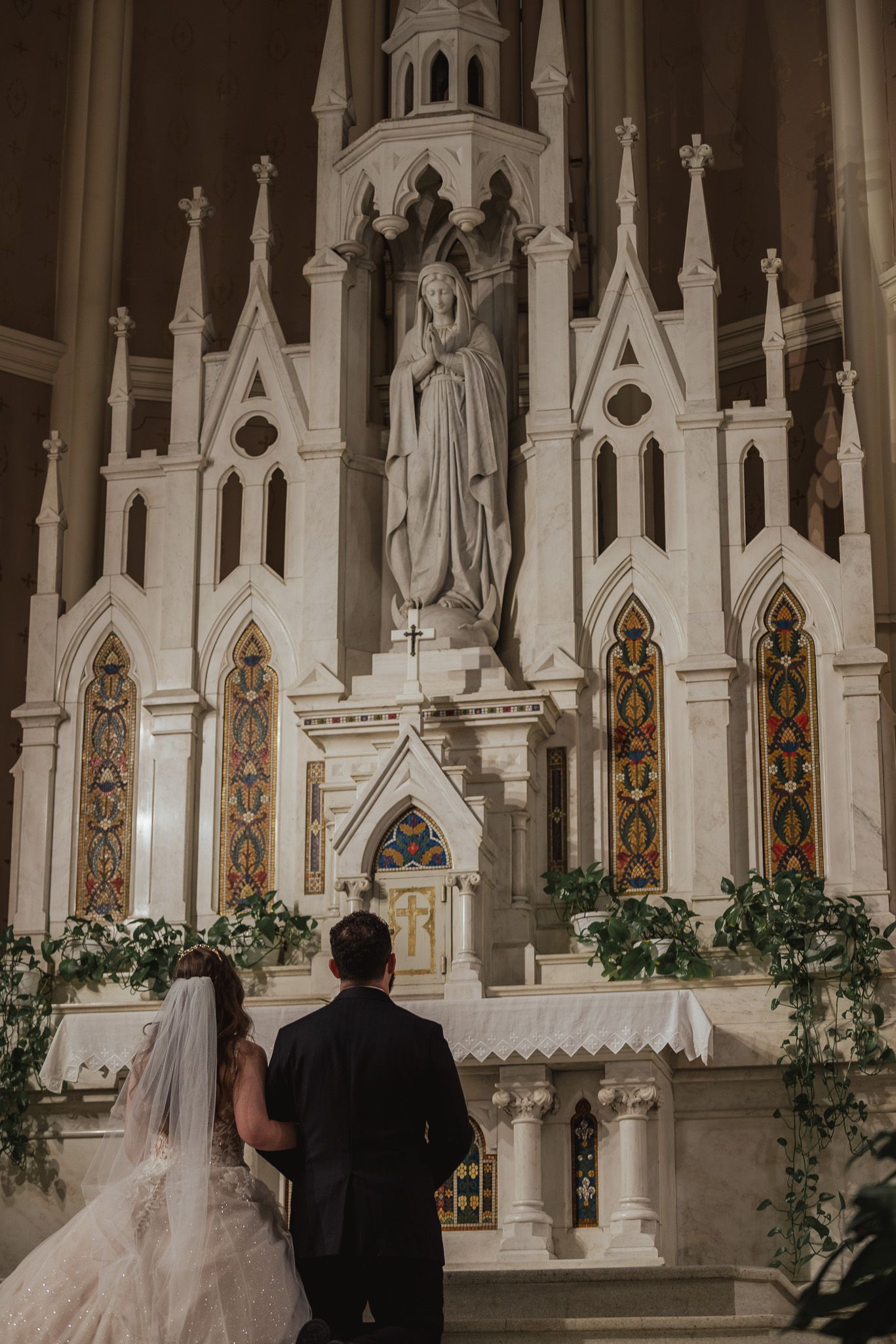 Wedding ceremony in a gothic cathedral with ornate white altar and stained glass windows.