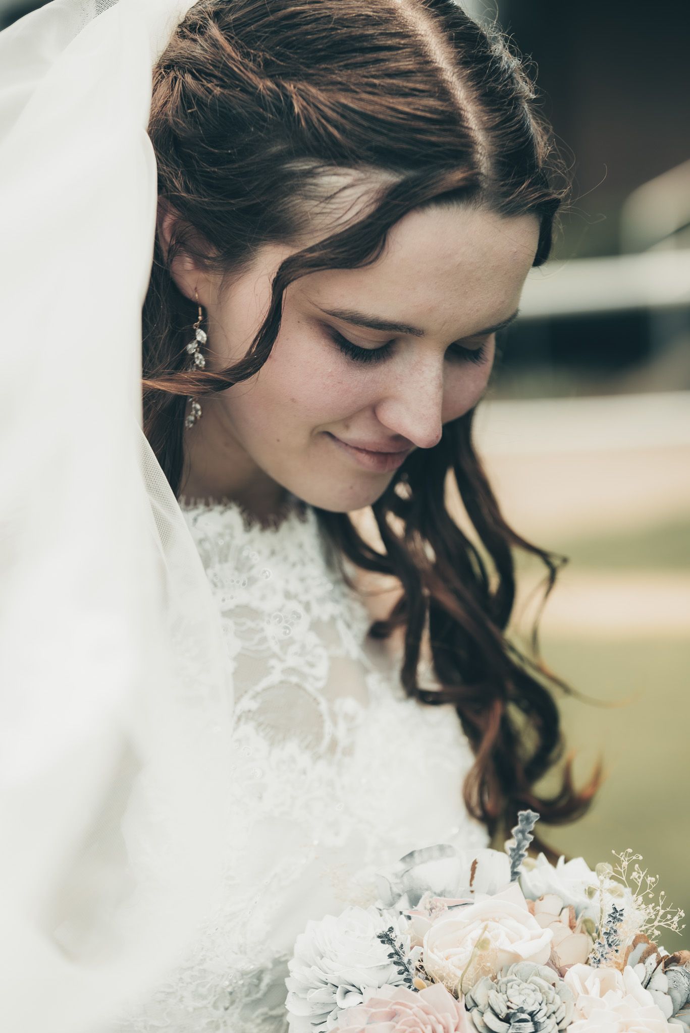 Close-up of bride in lace dress holding delicate pastel bouquet.