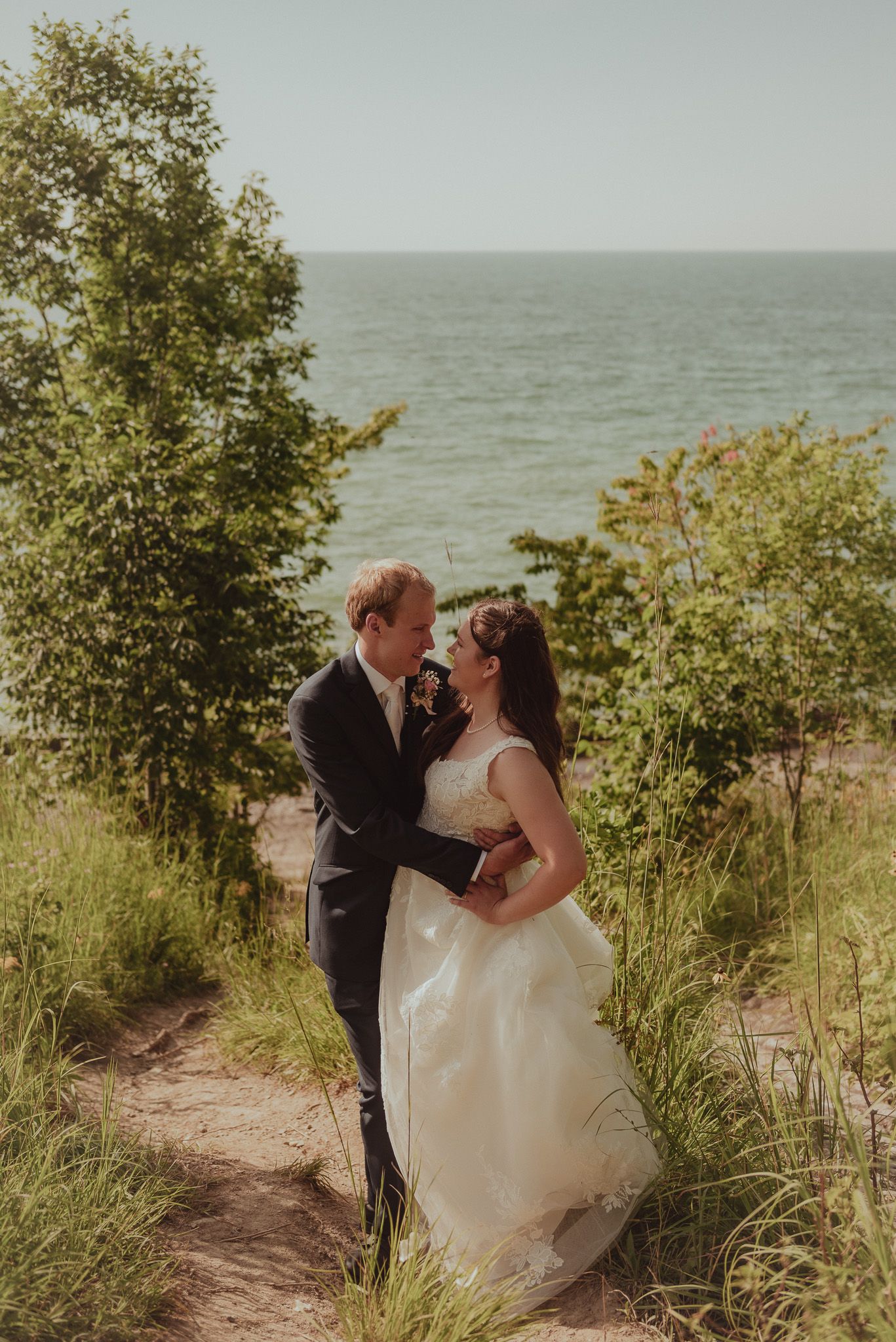 Romantic couple embracing on a beach cliff with ocean and greenery in background.