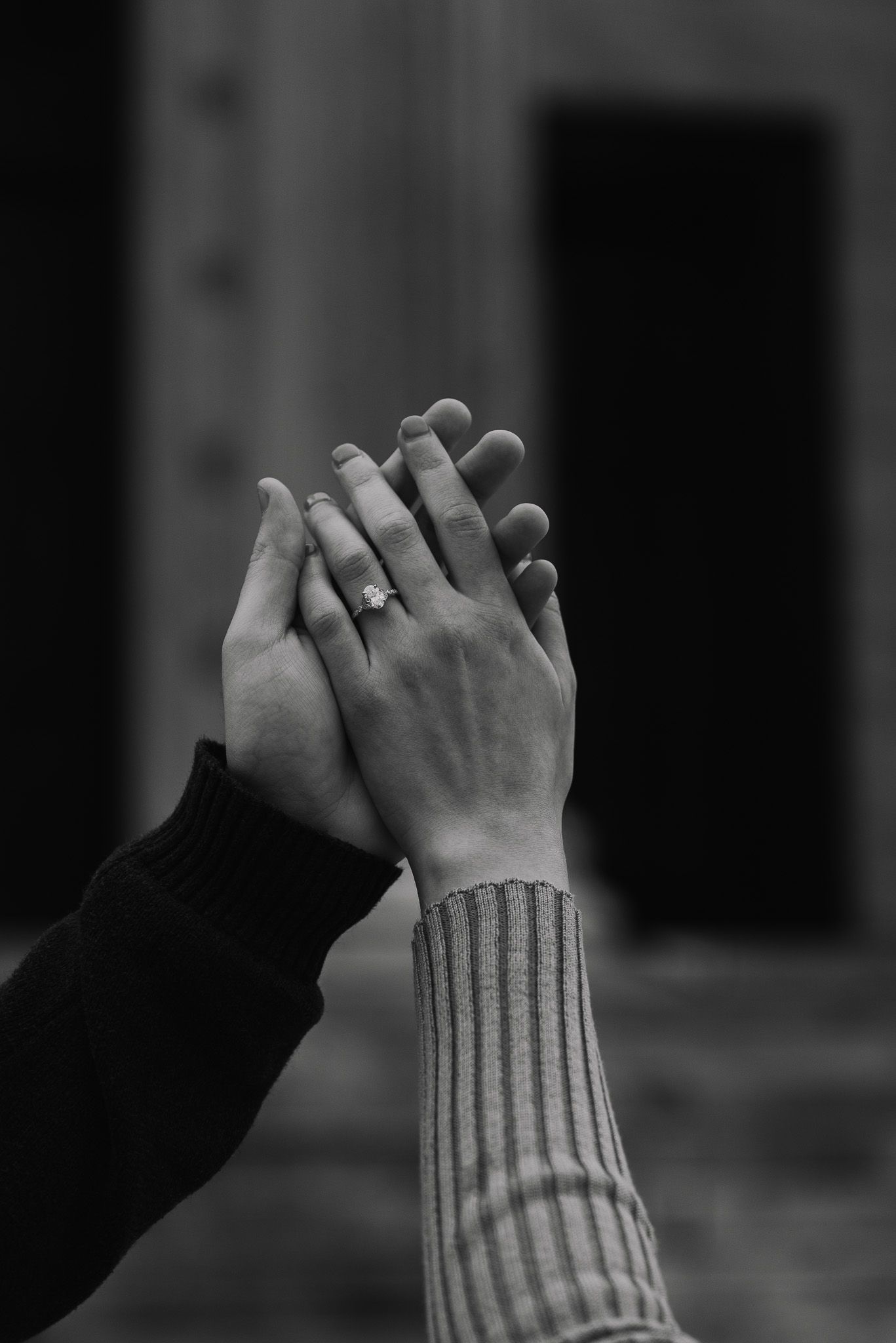 Black and white close-up of two hands clasped together showing an engagement ring.