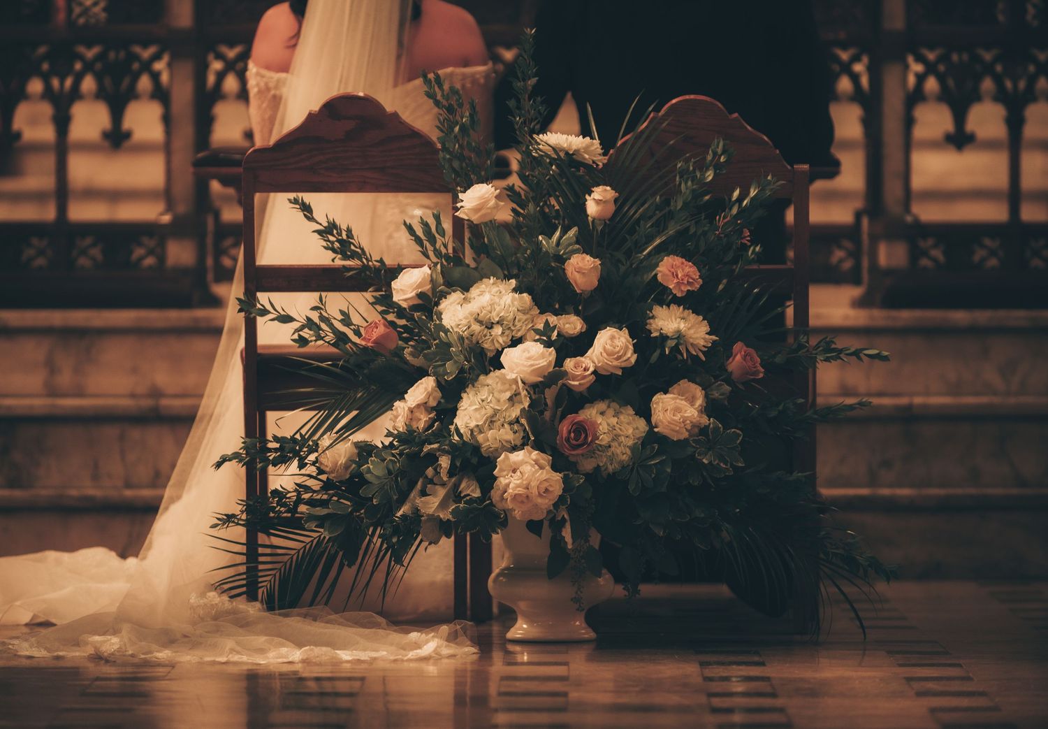 Elegant floral arrangements with white roses decorate a church altar during a wedding ceremony.