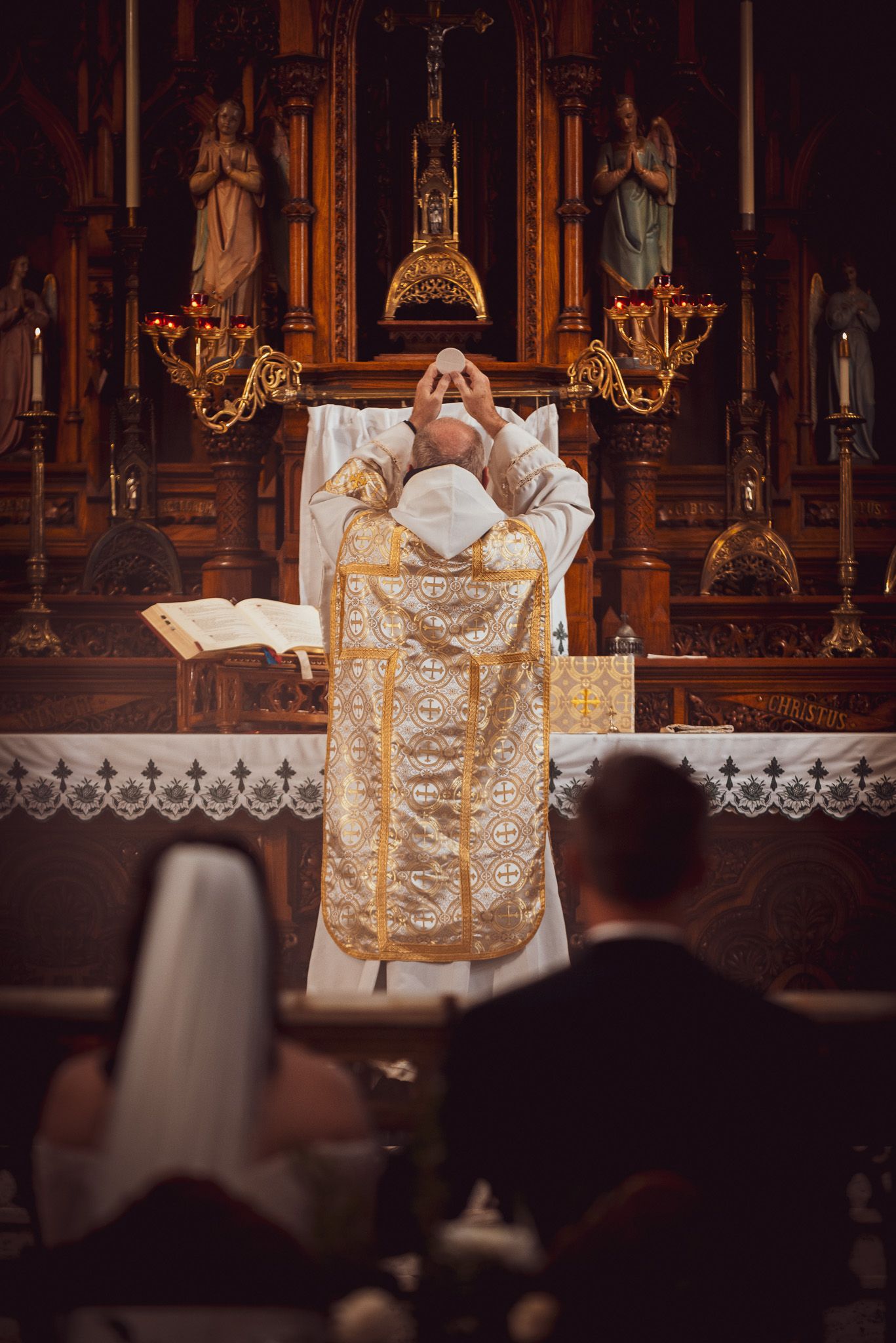 Priest in gold vestments elevates the Eucharist during Traditional Latin Mass.