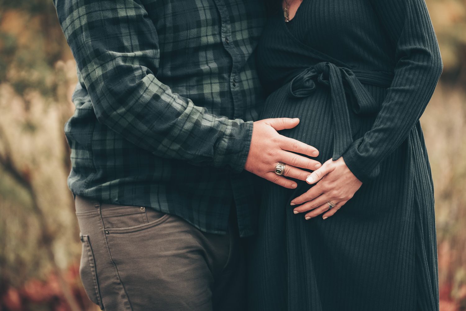 Close-up shot of hands cradling a pregnant belly in warm natural lighting.