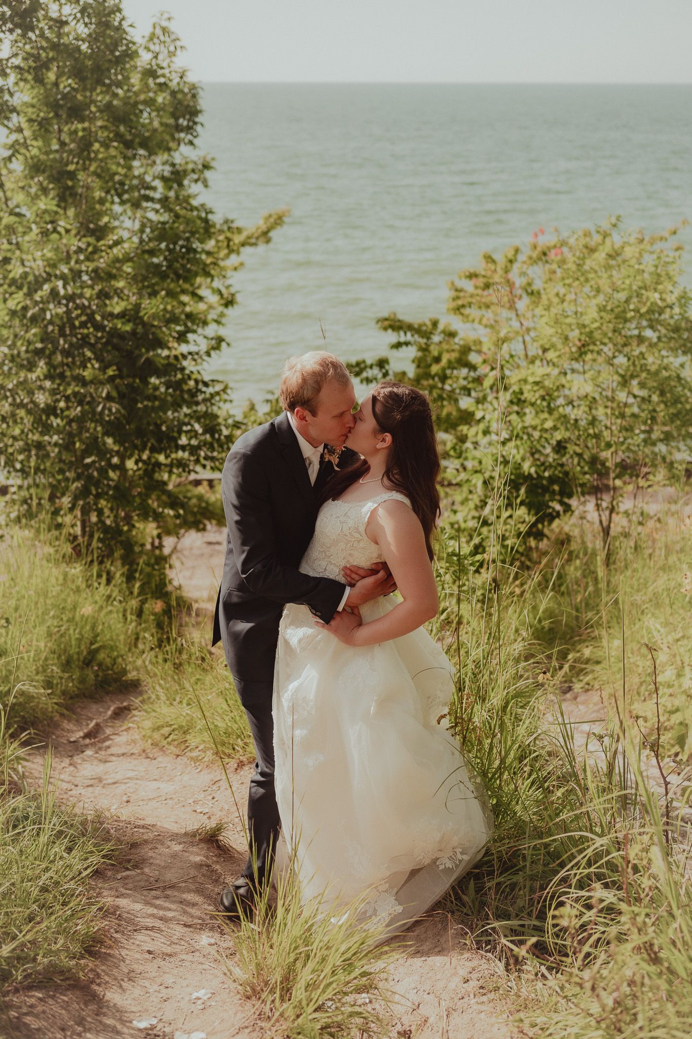 Newlyweds share romantic moments on a scenic beach path surrounded by greenery.
