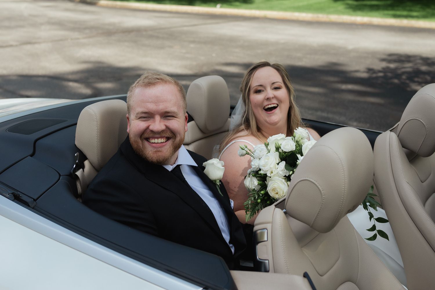 Newlyweds share joyful moment while riding in convertible car after wedding ceremony.