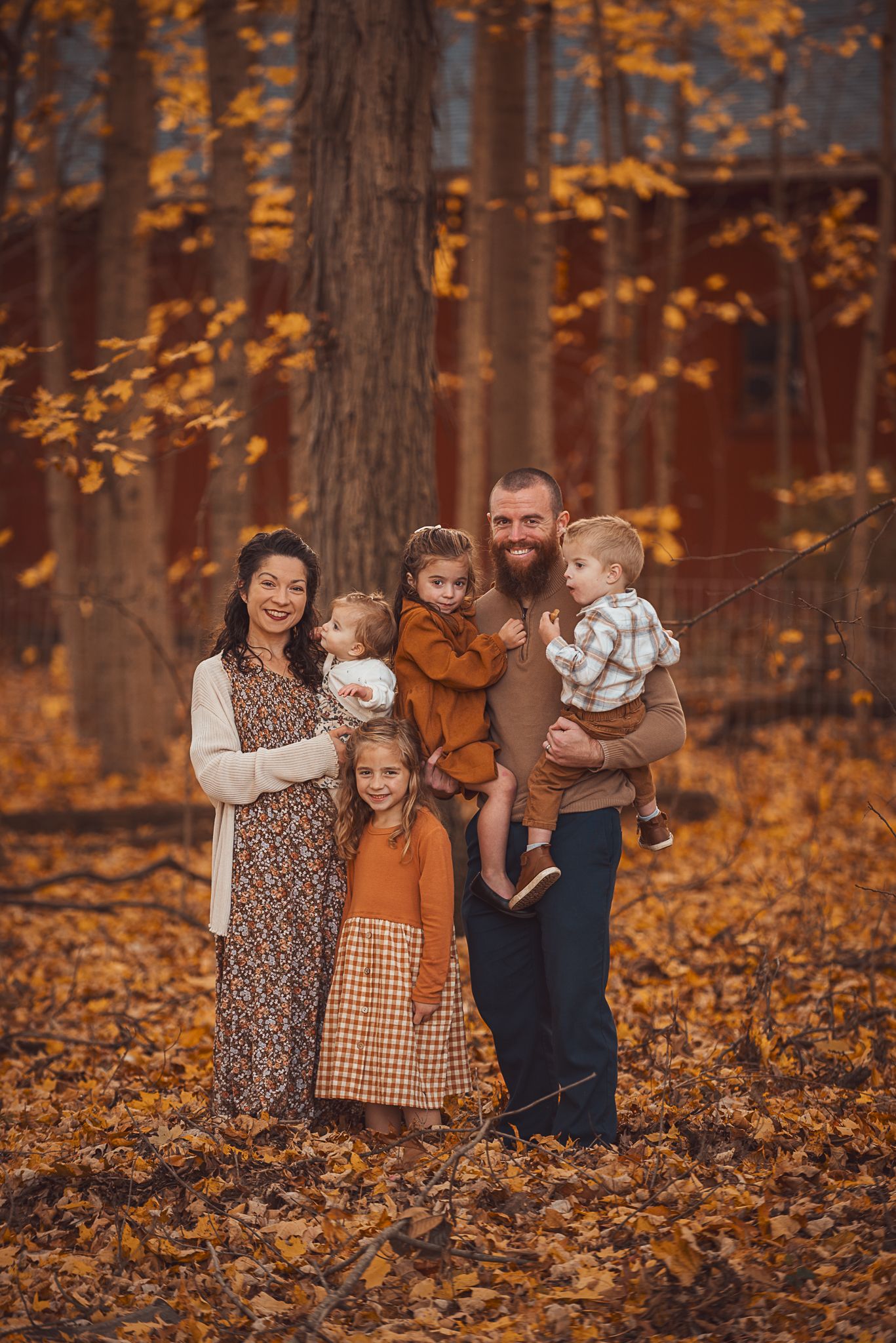 Family wearing autumn-colored clothing poses together in a forest filled with golden fall leaves.