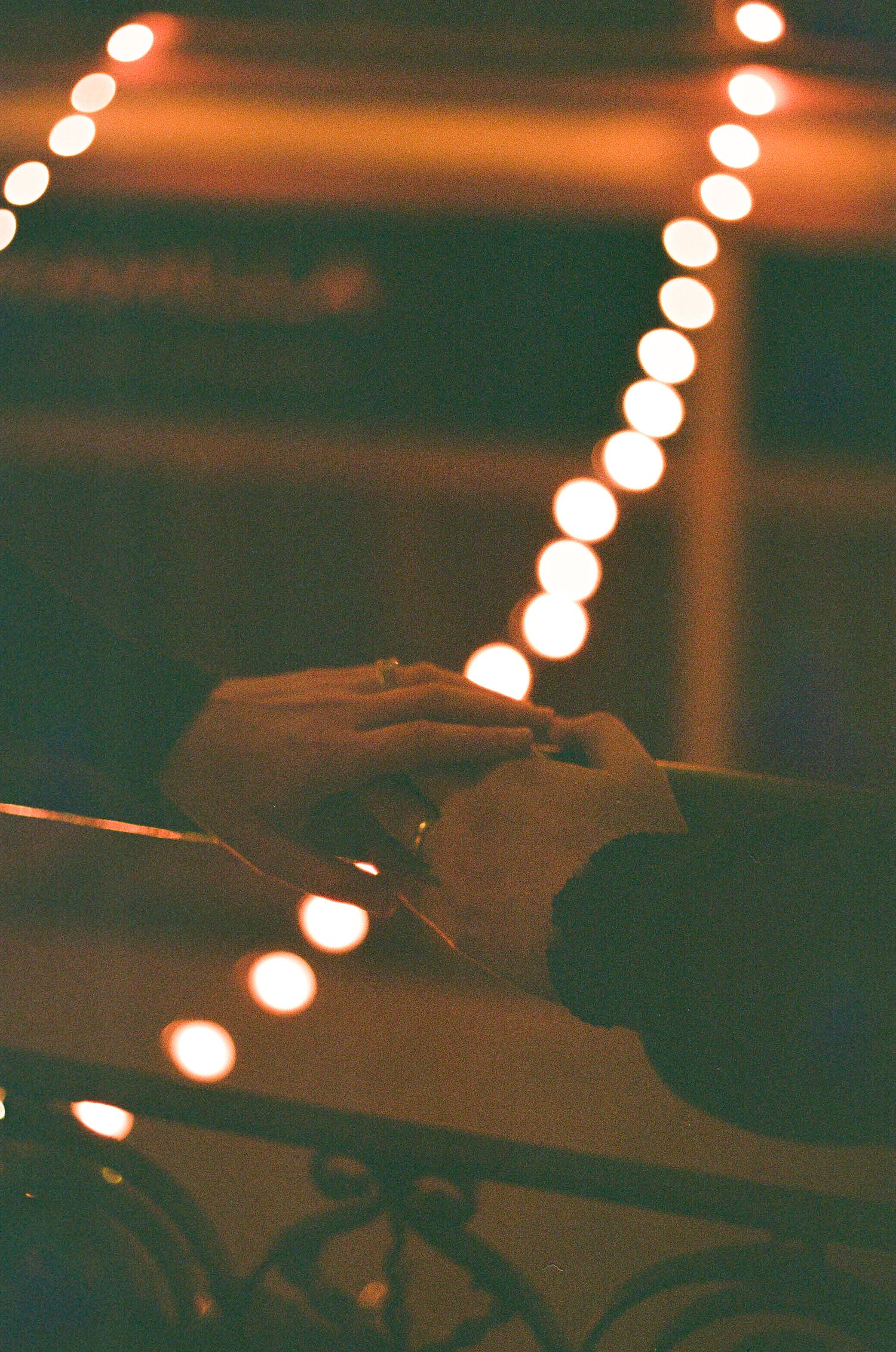 A string of glowing lights creates a bokeh effect above a dark silhouetted surface in a moody nighttime scene.