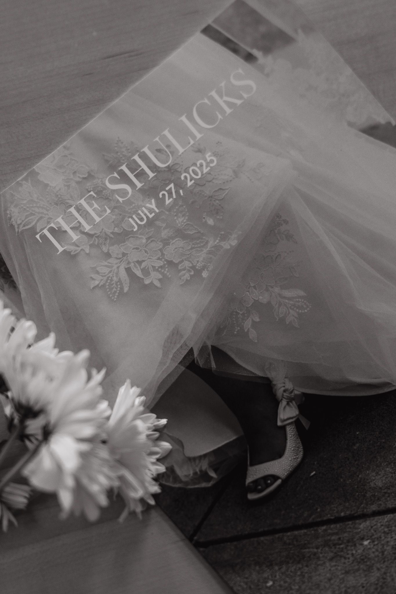 A black and white photo series showing a book with delicate tulle fabric and white flowers arranged on a dark surface.